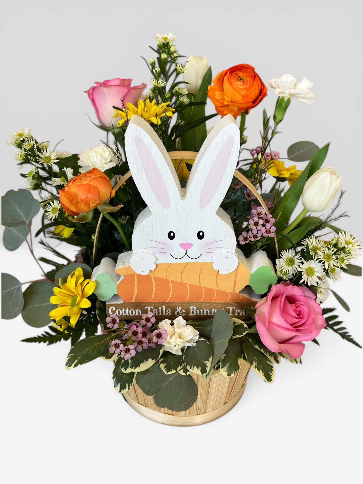 Hoppy Easter Bouquet  - Send the fun and joy of the holiday with our Hoppy Easter Bouquet. This Easter basket if filled with vibrant spring flowers, such as ranunculus, roses, daisies and tulips, and includes a cute bunny wooden shelf sitter to use year after year. Bunny is 8" by 8". Approximate arrangement size is Standard 14" tall by 12" wide, Deluxe 16" tall by 14" wide, Premium 18" tall by 15" wide