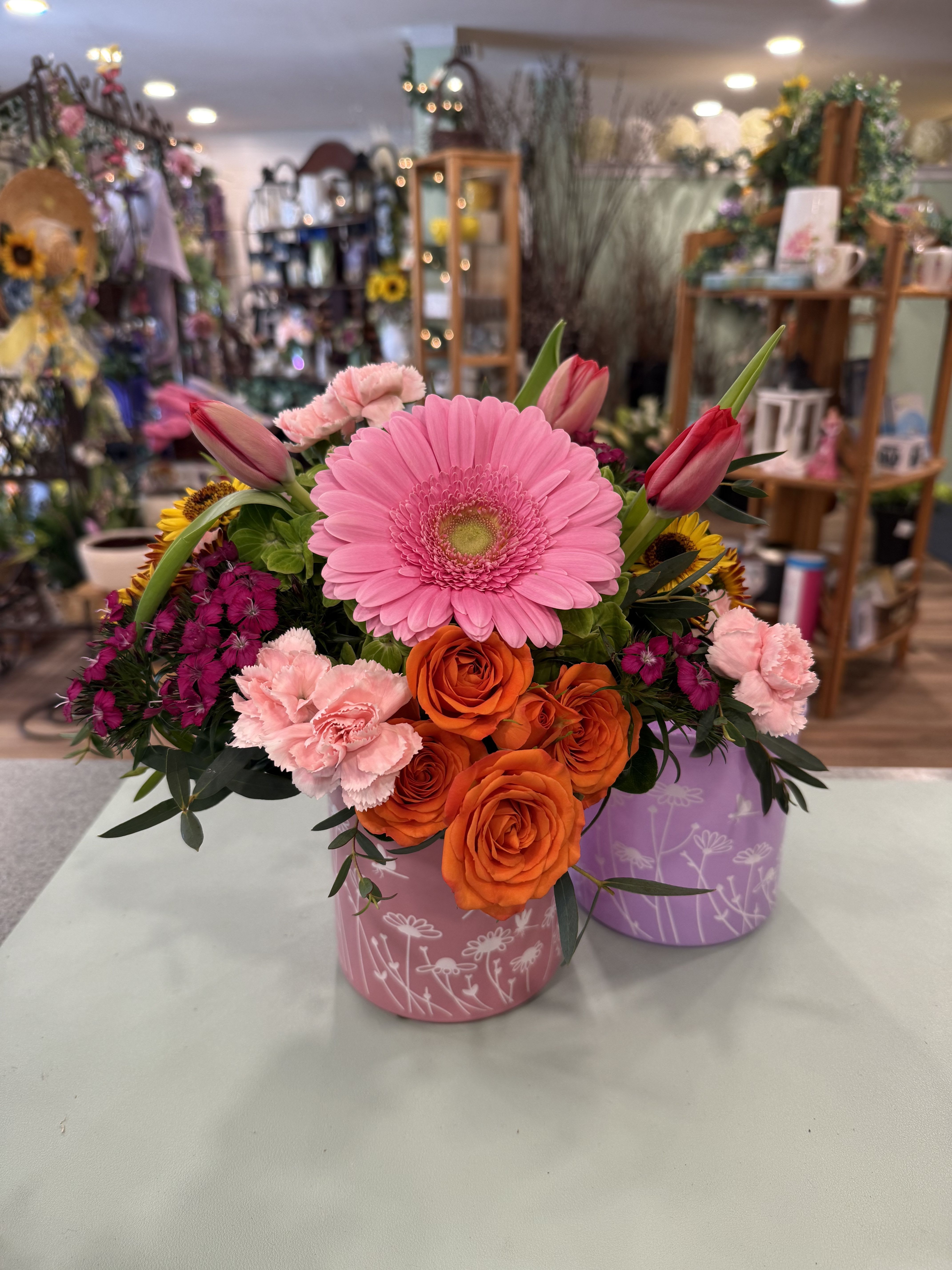 Spring Cylinder (SPC) - Green hydrangea, tulips, mini carnations, Viking mums, sweet William, spray roses &amp; a Gerber daisy make up this cheerful design. Arranged in a glass cylinder with floral emblems. Approx. 12 in tall.  ***Cylinder color may vary between pink or purple.  ***Flower type/color may vary depending on availability. 