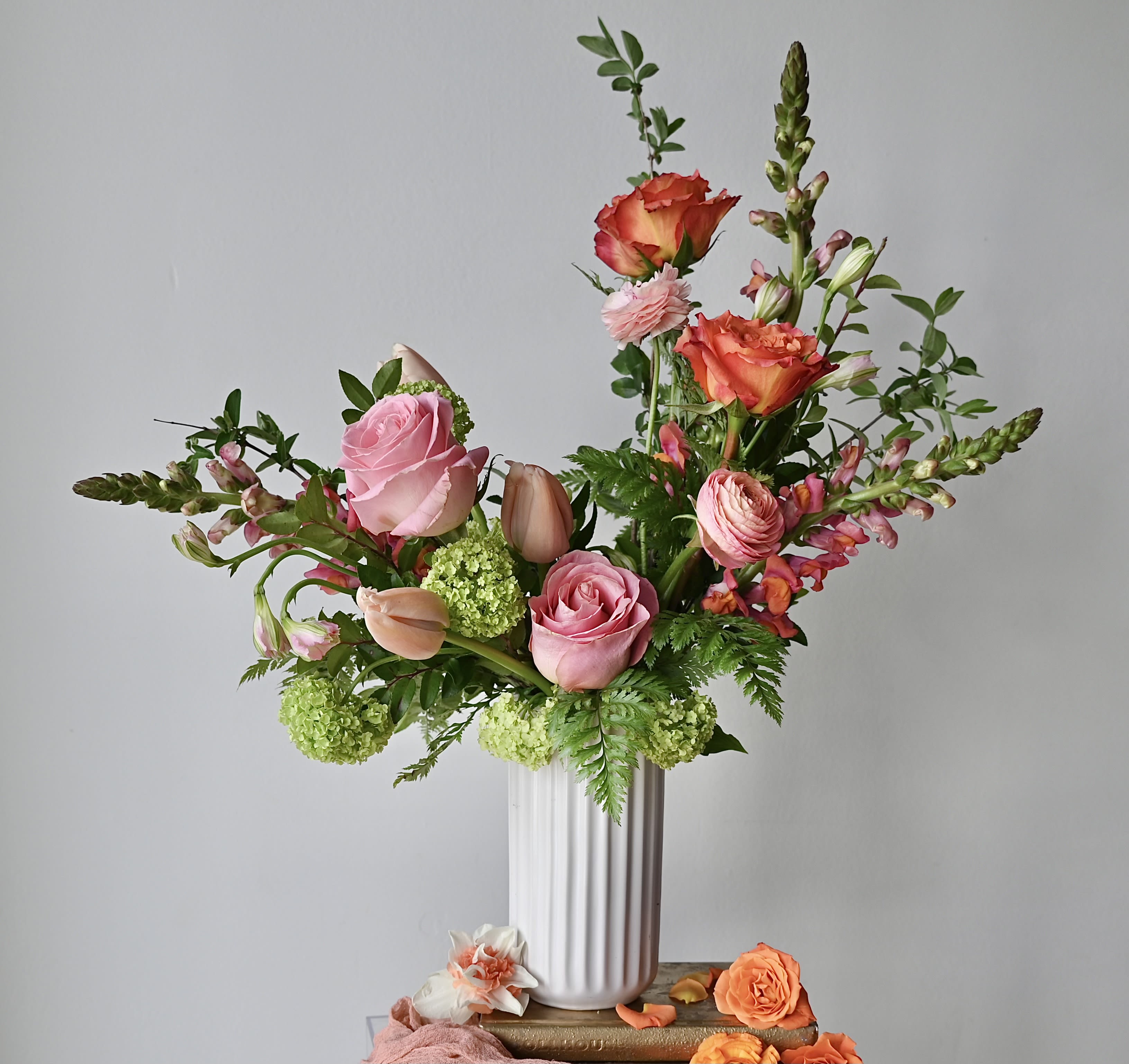 Darling Mama - A sweet and elegant tribute to the one who does it all. Darling Mama is thoughtfully designed in a tall, modern white cylinder, filled with a lush, seasonal mix of blooms in soft, feminine tones. Choose from two styles: •	Standard – A beautifully composed, front-facing arrangement, perfect for placing against a wall or as a statement on a desk or console. •	Deluxe – A fuller, 360-degree design ideal for a dining table or centerpiece, stunning from every angle. The arrangement is boxed with white tissue and wrapped with our black logo ribbon.