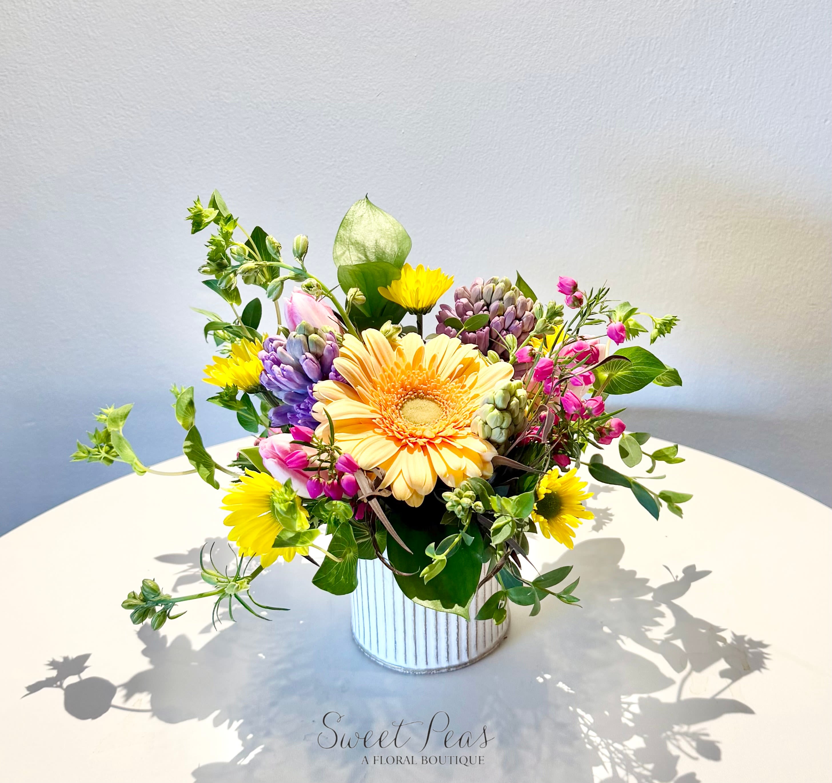 Easter Egg - Bursting with cheerful color and natural charm, Sunny Meadow Delight captures the joyful spirit of spring. Featuring a radiant gerbera daisy at its heart, this arrangement is accented with playful pops of yellow blooms, soft pastel tulips, delicate hyacinth, and airy garden greenery. Designed in a keepsake container, it brings the feeling of a sunlit meadow indoors—perfect for celebrating the season, brightening someone’s day, or simply adding a touch of fresh spring beauty to any space.