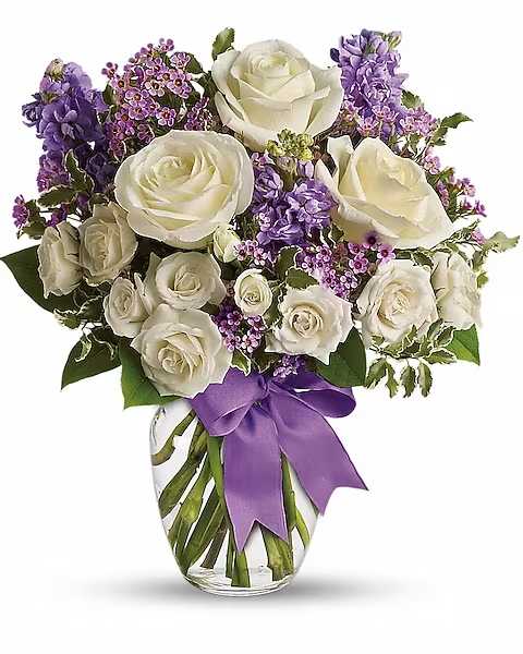 Clear vase of white roses and purple flowers tied with a purple ribbon bow
