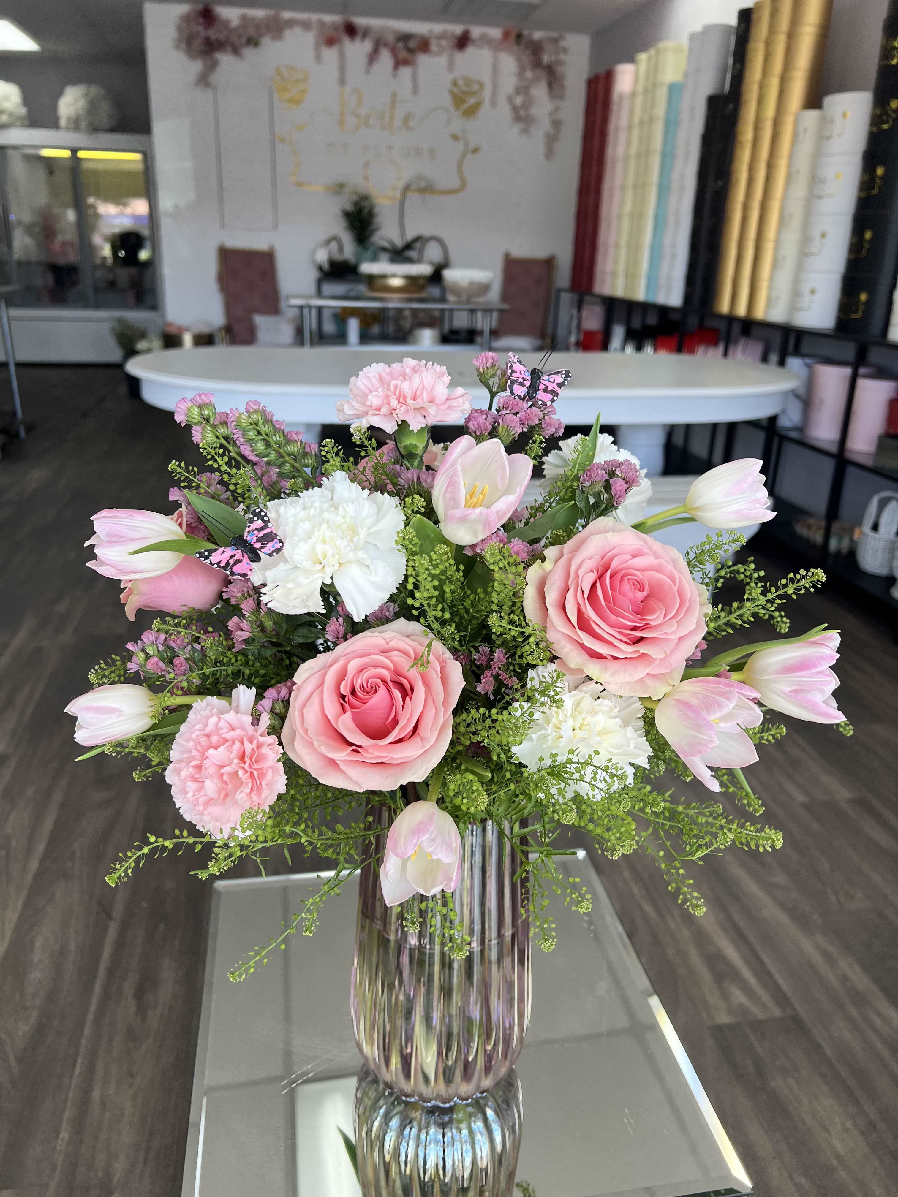 Spring in Bloom - A dreamy flower vase arrangement featuring soft pink roses, delicate tulips, and ruffled carnations, accented with airy green lepidium and charming butterfly details. Designed in a modern glass vase, this spring flower arrangement is perfect for birthdays, anniversaries, special events or just because. 