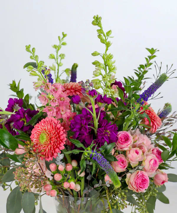 Mixed bouquet of pink and purple flowers with green spikes in a clear glass vase