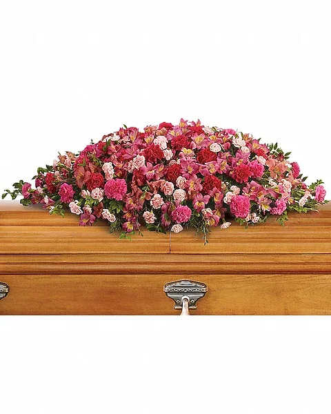 Pink and red casket spray of mixed flowers arranged on a light wood casket