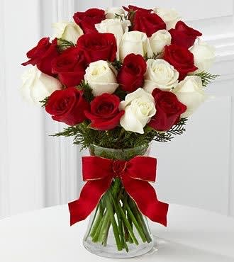 Arrangement of red and white roses in a clear vase with a red bow