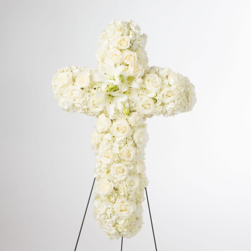Standing cross-shaped spray of white roses, lilies, and hydrangeas on a metal easel.