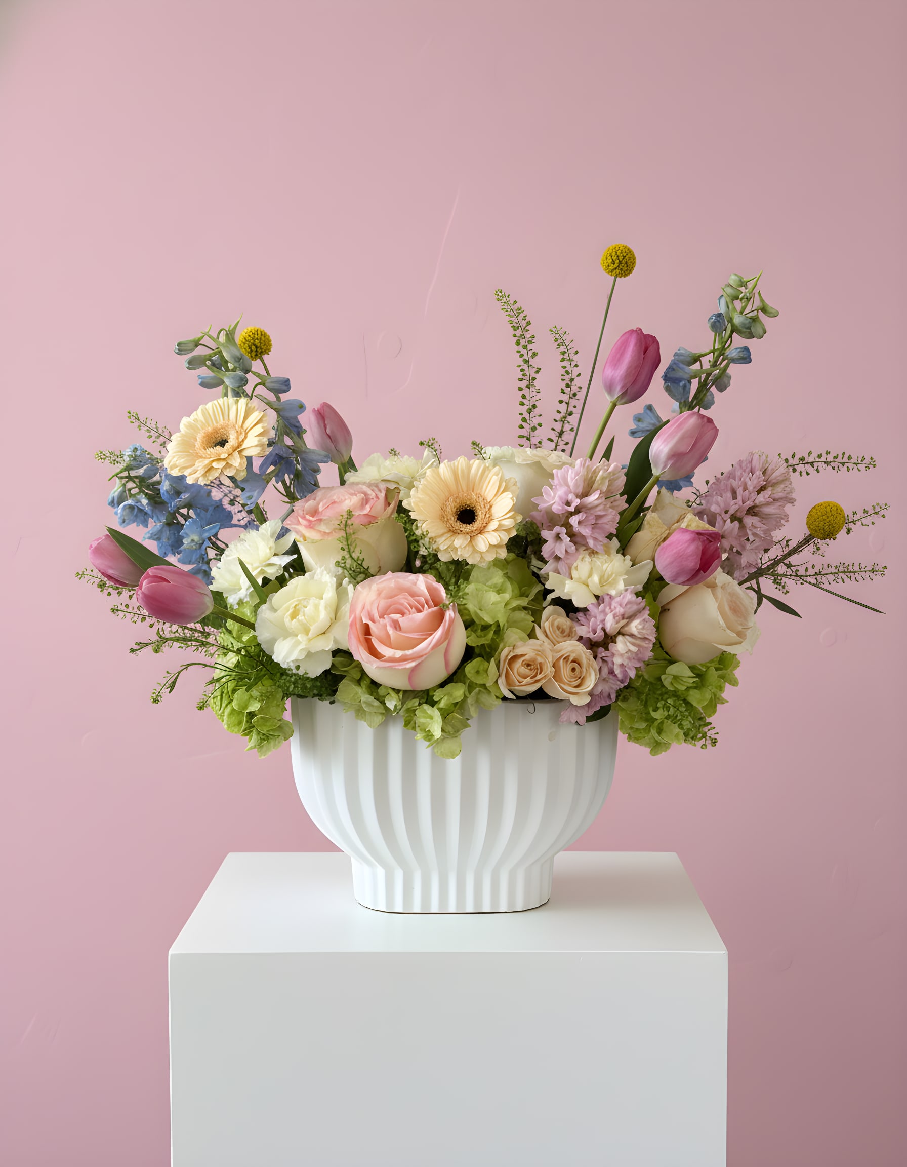 Spring Garden - A mix of blush roses, tulips, gerberas, and seasonal blooms in pastel tones, arranged with fresh greenery in a white vase.