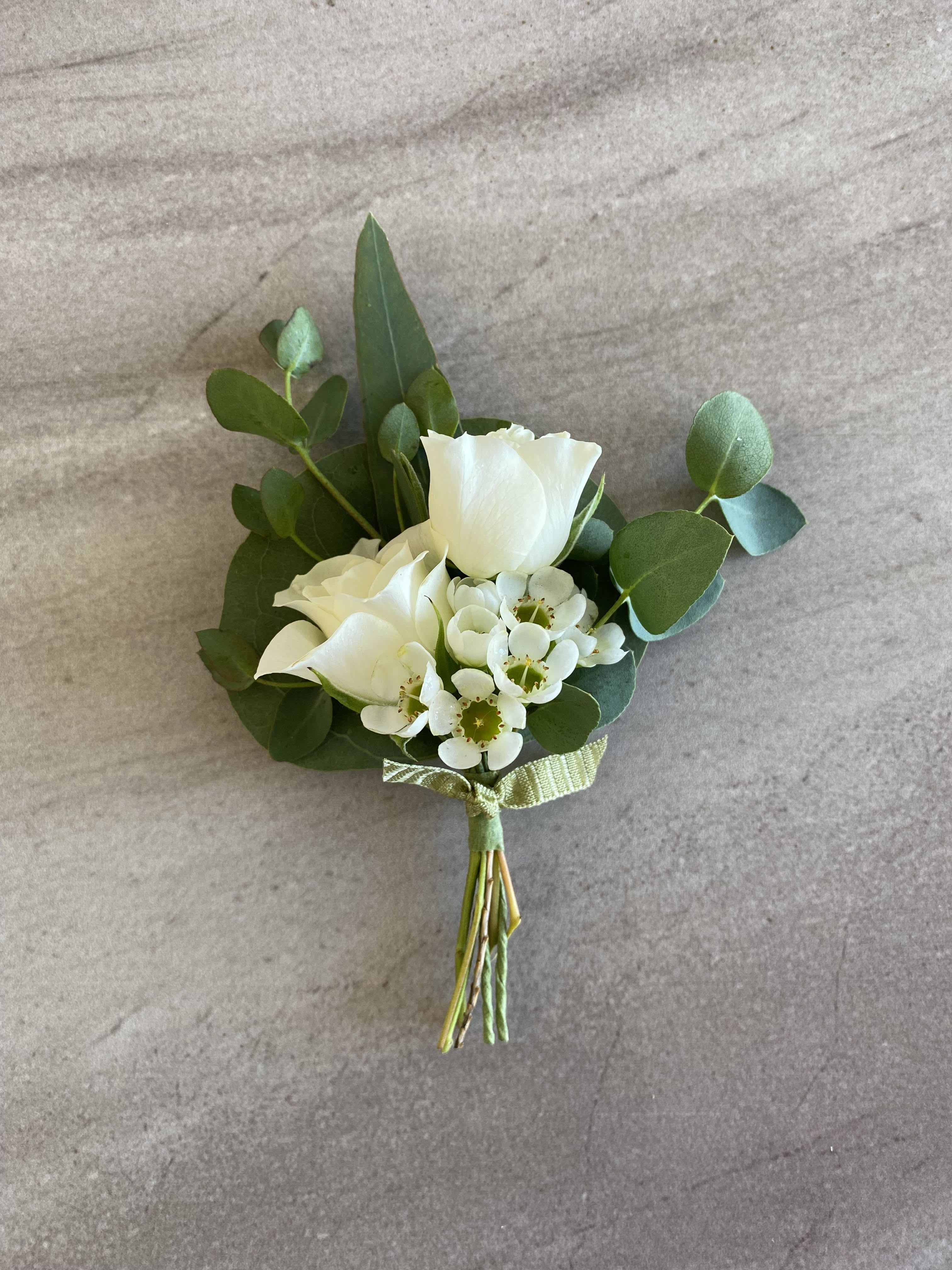 Small white rose boutonniere with tiny white accent flowers and a green ribbon tie