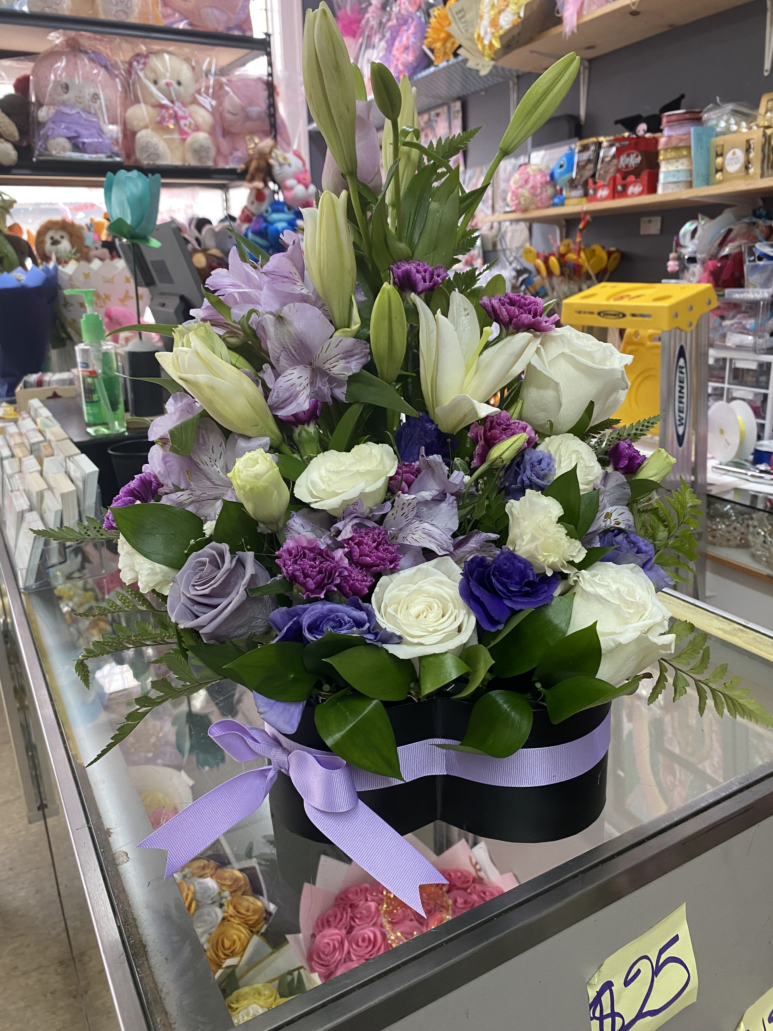 Lavender and white flower arrangement with roses, lilies, and carnations in a black hatbox with purple ribbon