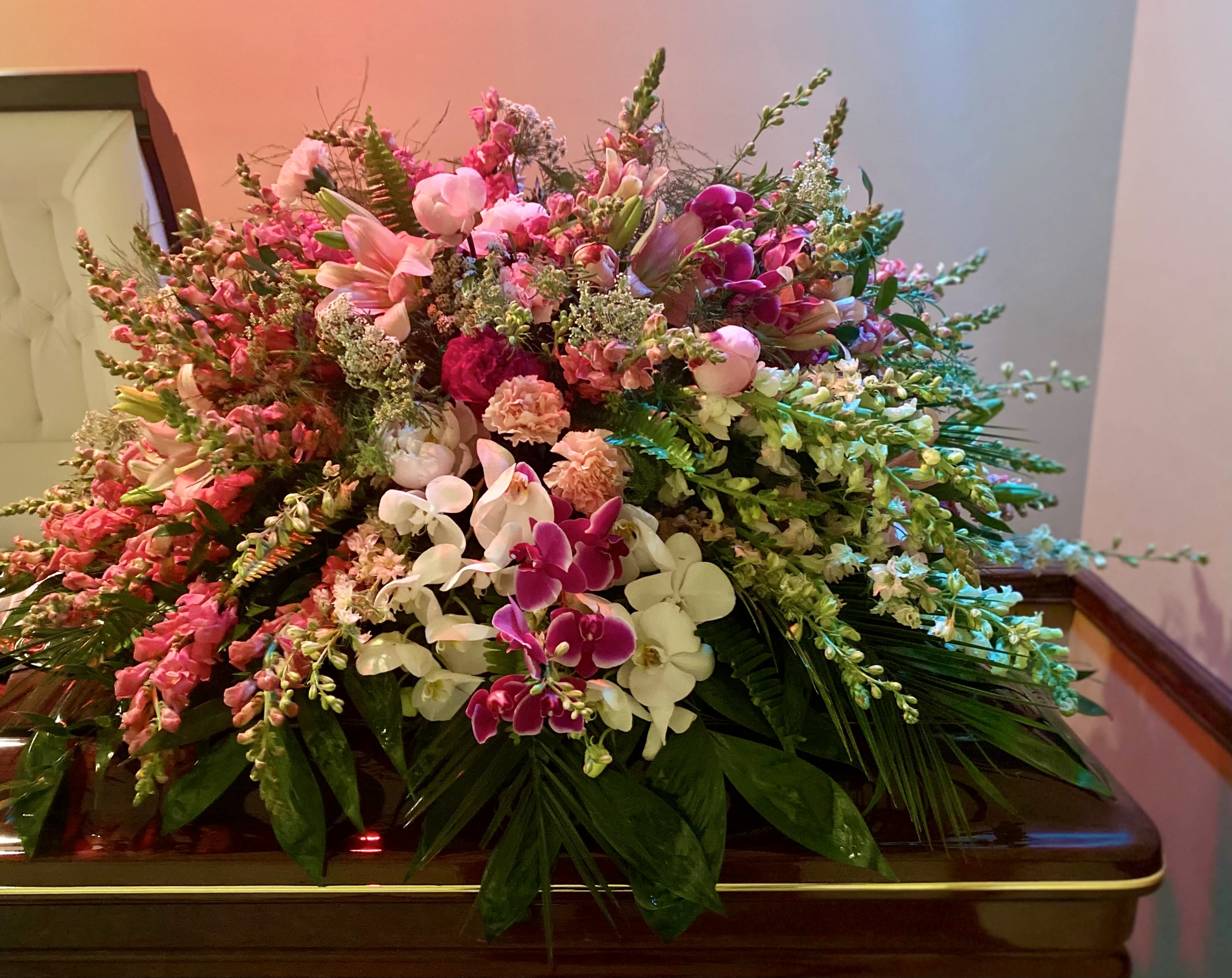 Large pink and white flower casket spray with orchids and lilies on a closed wooden casket