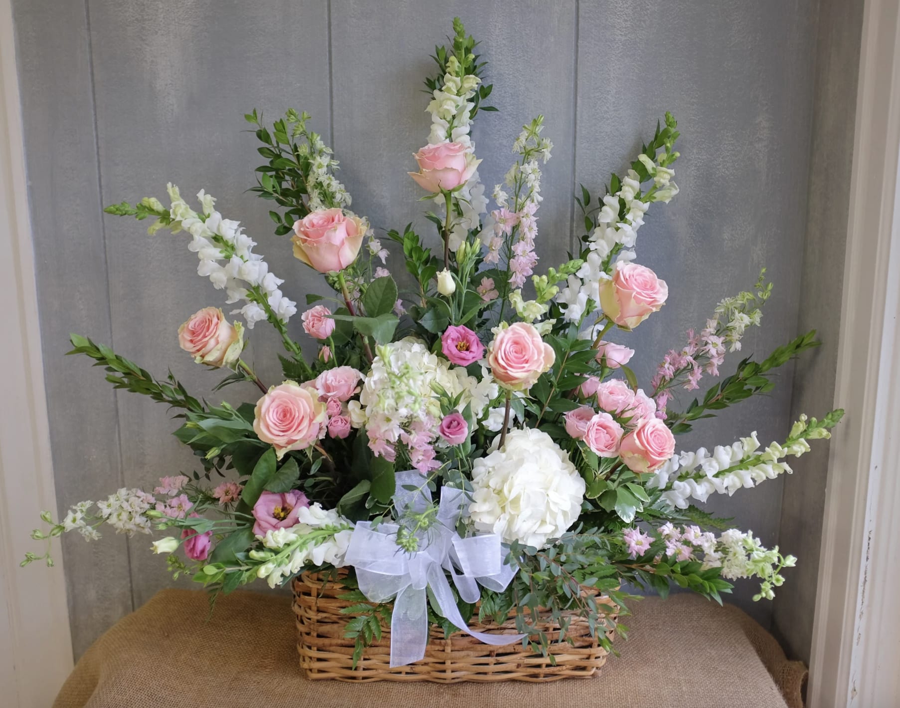 Fan-shaped basket arrangement of pink roses and white flowers with a white bow