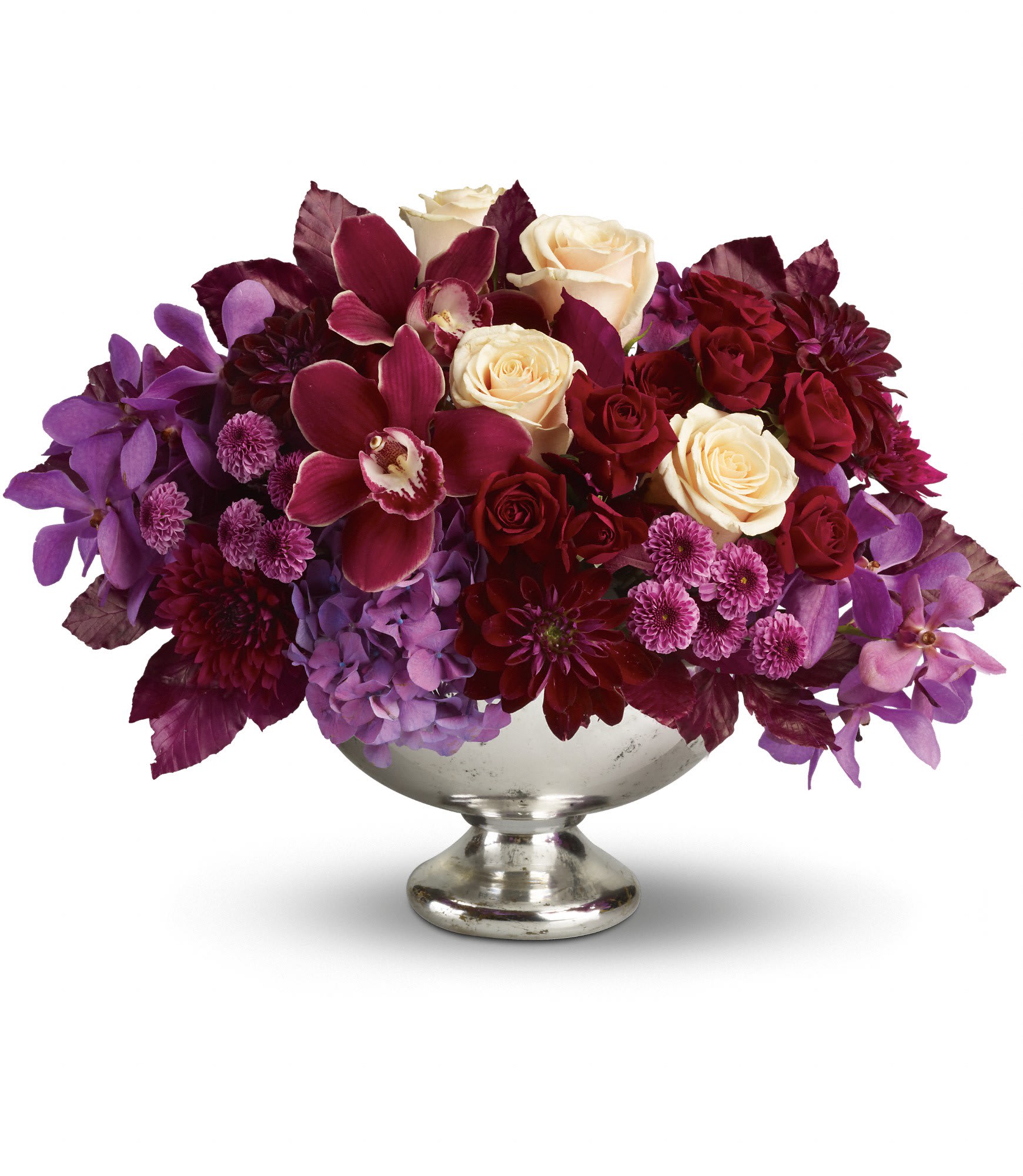 Low arrangement of cream roses, burgundy blooms, and purple flowers in a silver pedestal bowl
