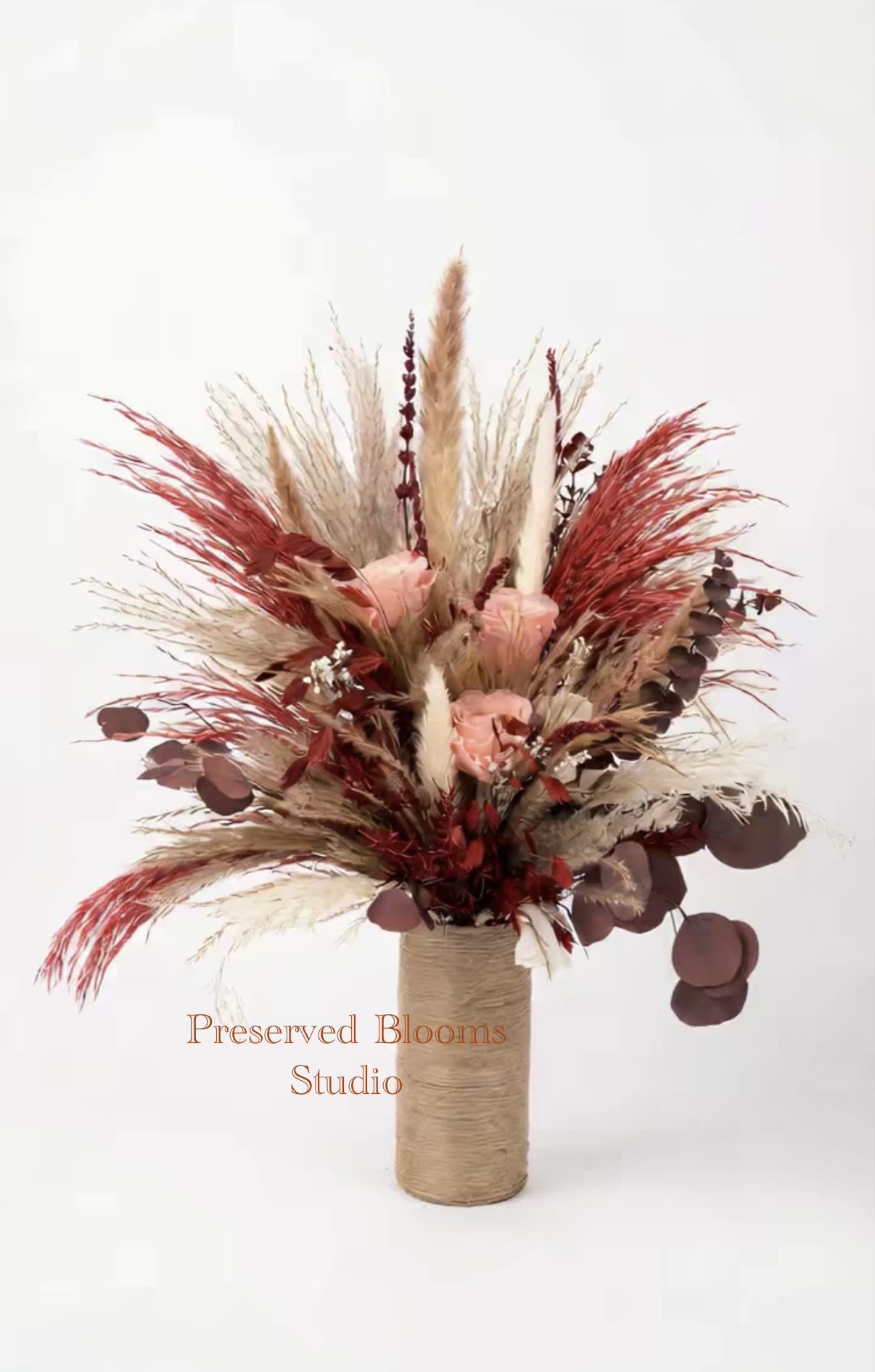 Tall dried arrangement with peach roses, red and tan pampas plumes in a twine-wrapped cylinder vase