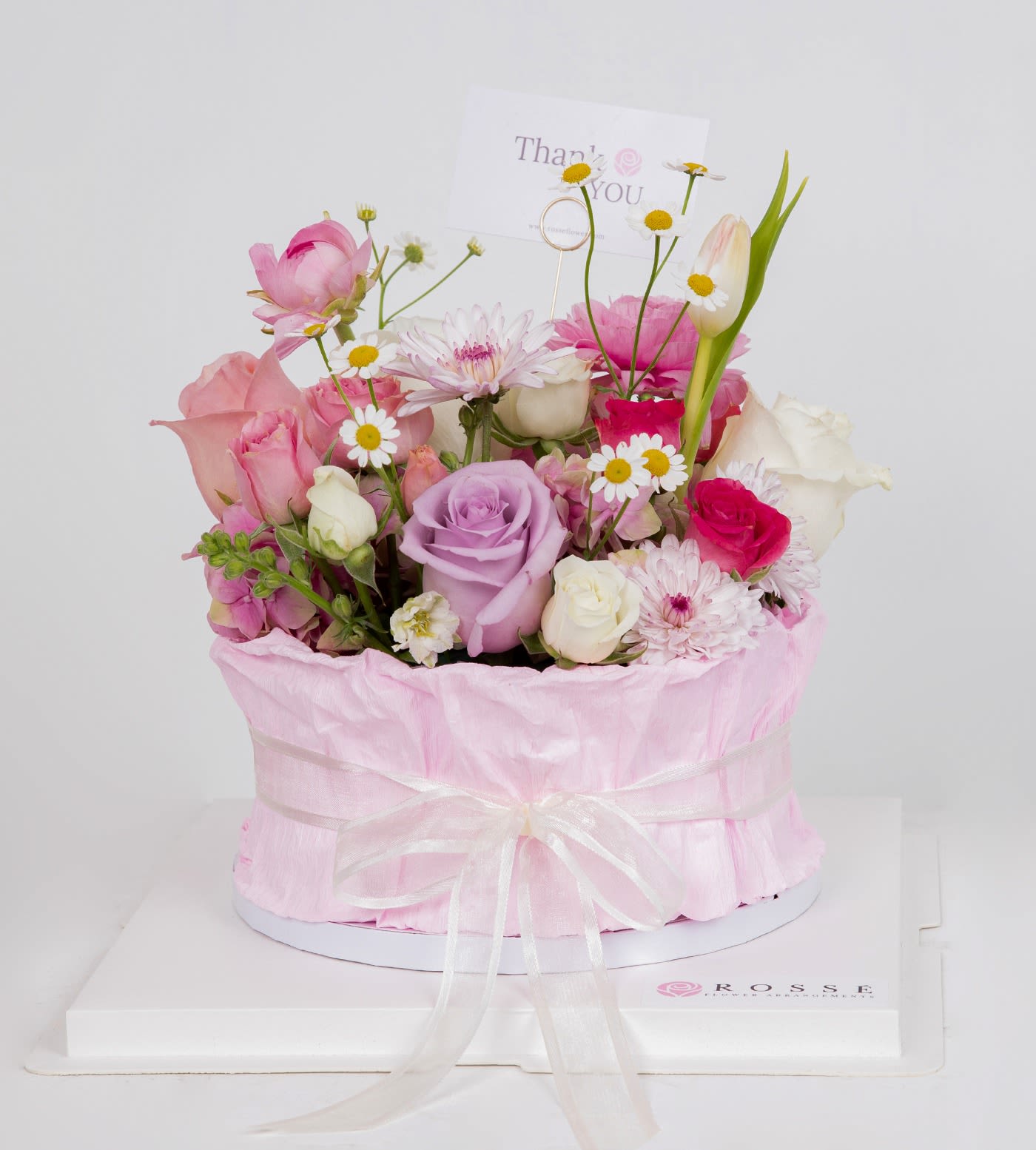 Pastel pink and lavender mixed flowers in a round pink hatbox with a thank you card.