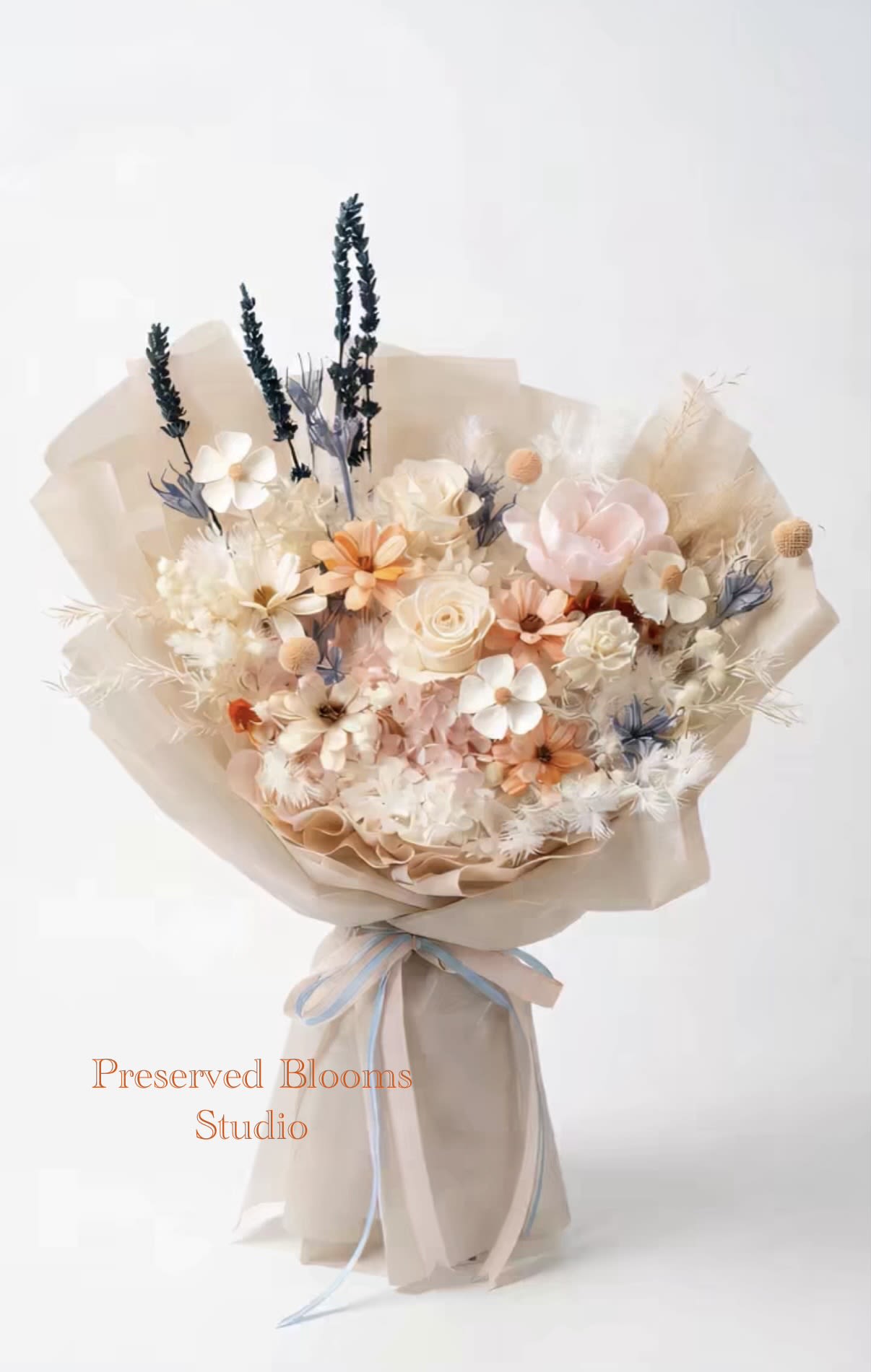 Pastel bouquet of preserved flowers wrapped in beige paper with blue and peach ribbon.