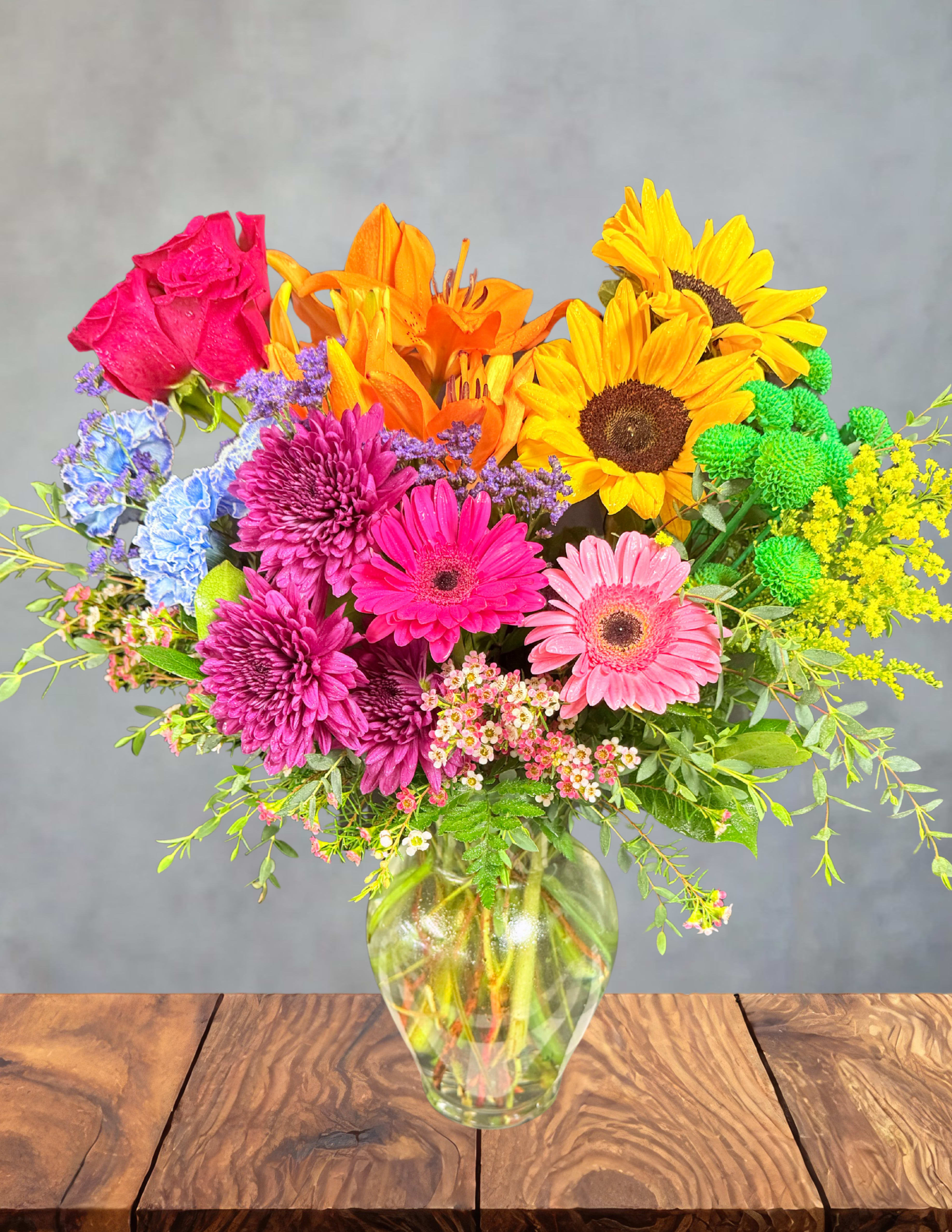 Garden of skittles  - A joyful explosion of color, Skittle Garden is where every bloom feels like a piece of sunshine‑flavored candy. Bursting with vibrant pinks, purples, yellows, oranges, and blues, this arrangement brings the full rainbow to life in a way that’s bold, cheerful, and impossible to ignore. Sunflowers beam, lilies glow, daisies pop, and hydrangeas add that perfect splash of cool sweetness — all nestled in lush greenery for balance.