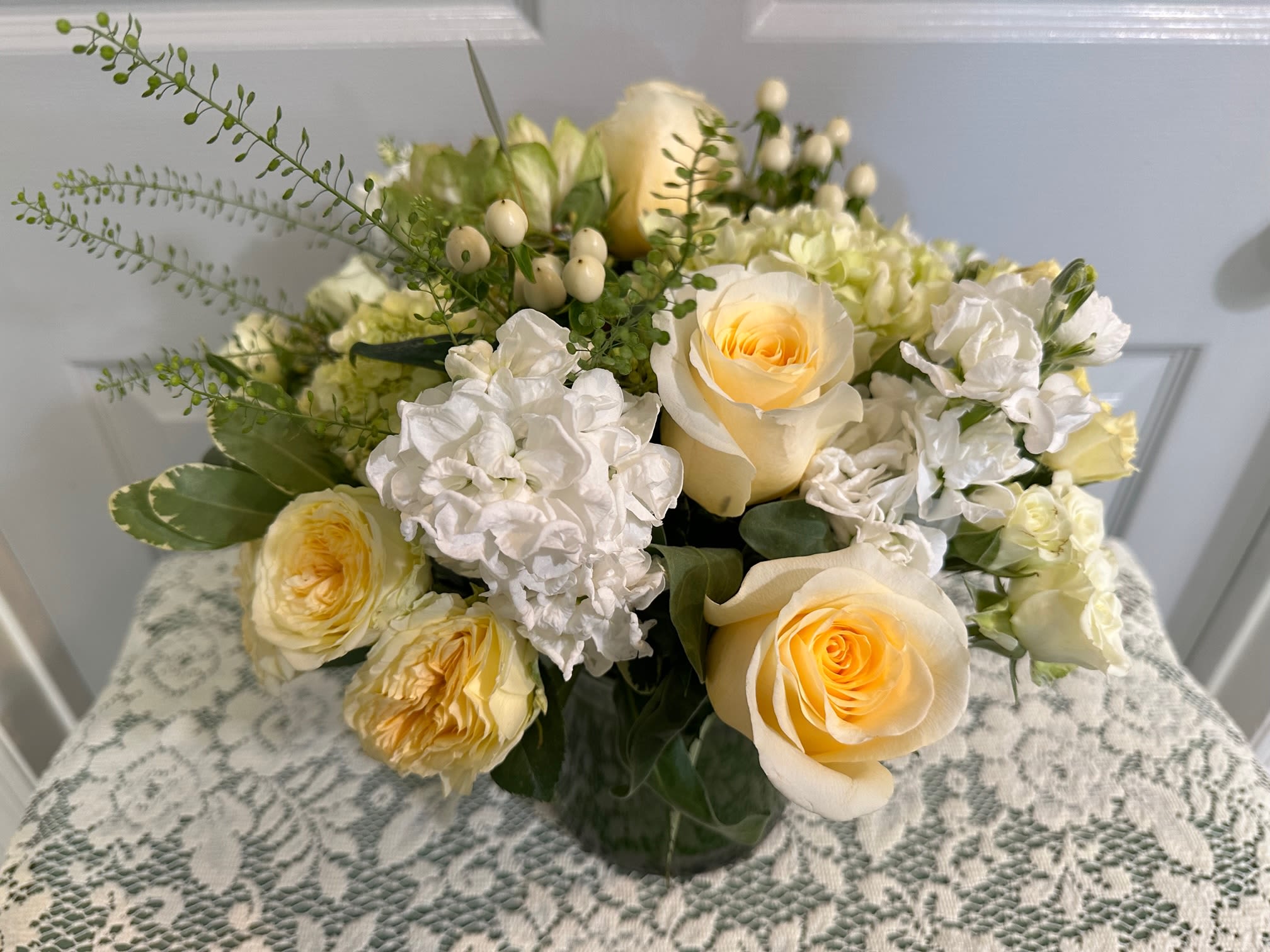 Low glass vase of pale yellow roses and white stock in a rounded arrangement