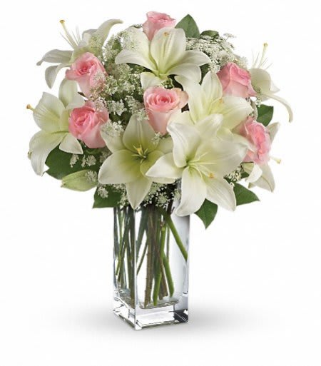 Tall glass vase arrangement with white lilies, pink roses, and delicate white filler flowers.