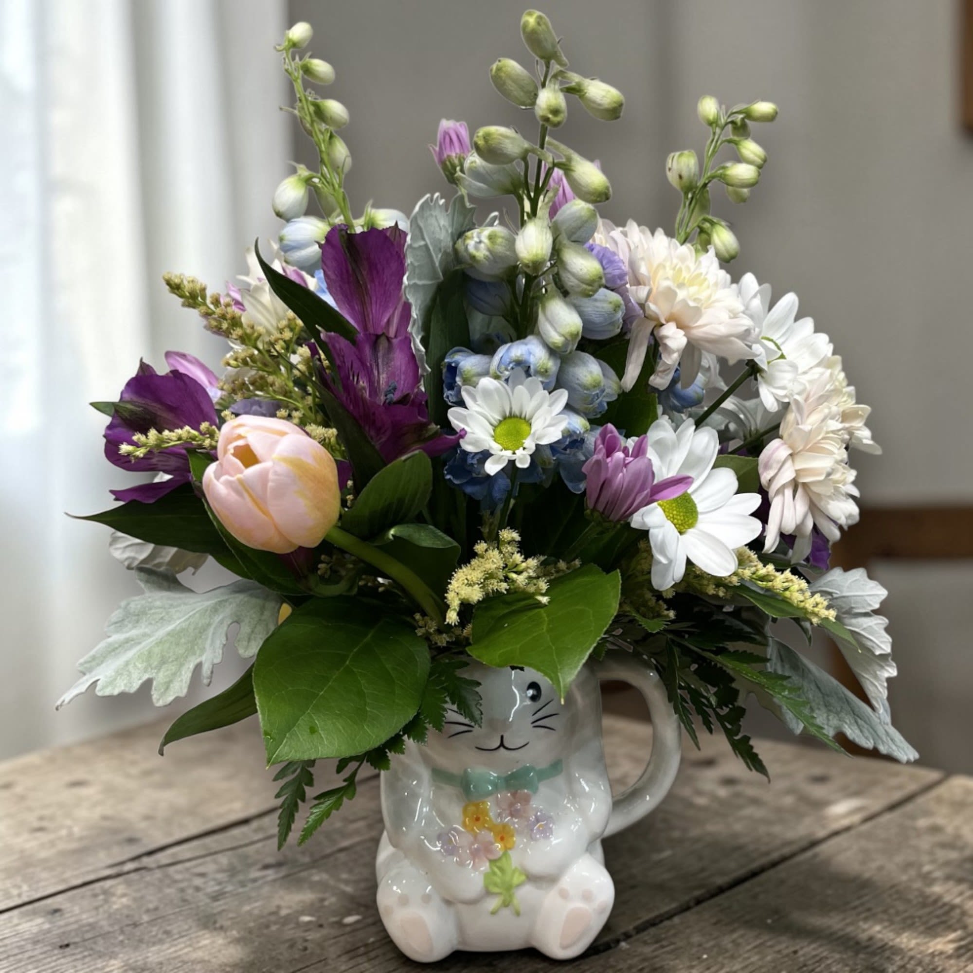 Cup O' Bunny - An adorable bunny mug filled with a generous mix of spring blooms, cheerful tulips, daisies, and seasonal accents.