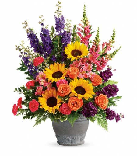 Bright arrangement of sunflowers, orange roses, and mixed pink and purple flowers in a gray pot