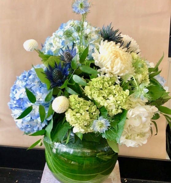 Summer on Nantucket - Imagine being on vacation in Nantucket and walking along hydrangea lined sidewalks. This stunning arrangement reminds you of just that, consisting of blue and green hydrangea, white football mums, mini pom pom dahlia, and thistle.