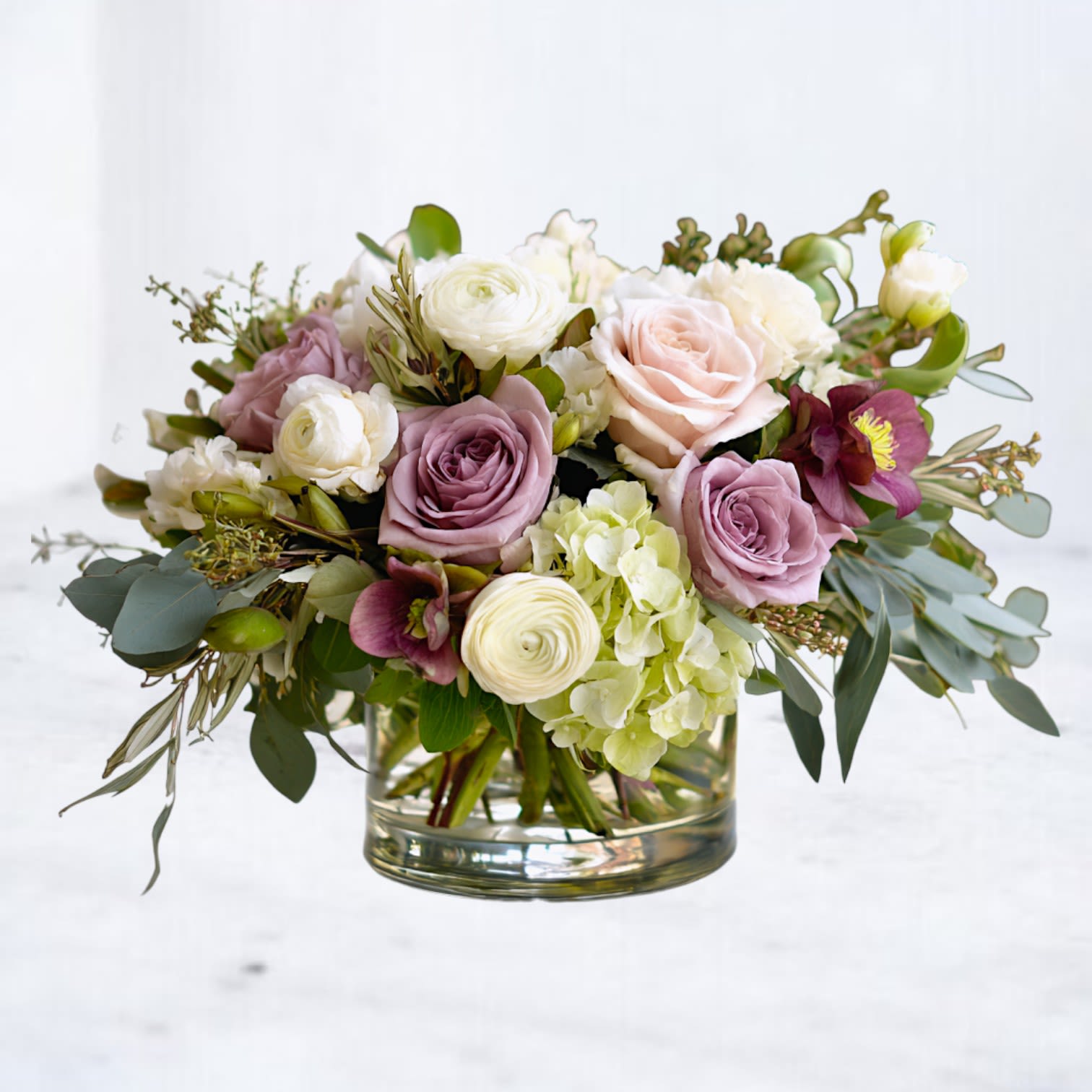 Low arrangement of pastel roses, ranunculus, and green hydrangeas in a clear glass vase
