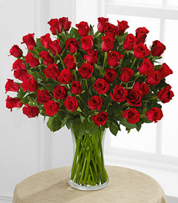 Large bouquet of long-stemmed red roses arranged in a clear glass vase on a round table