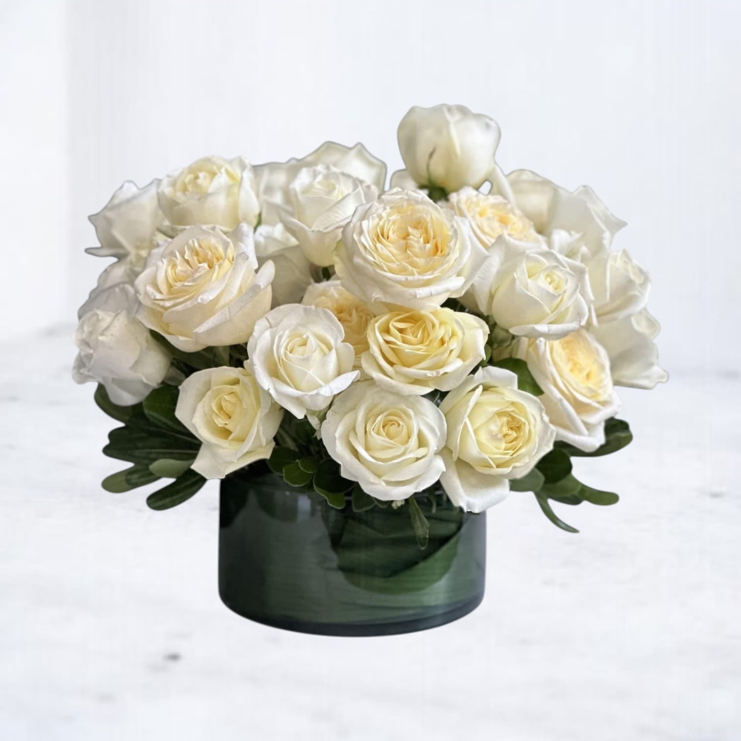 Low arrangement of white and cream roses in a dark green glass cylinder vase