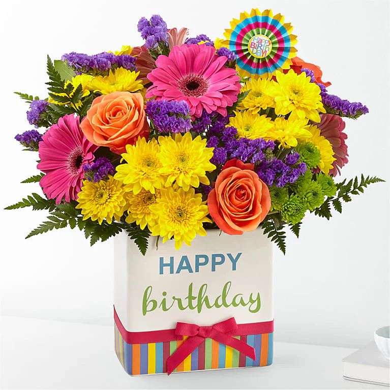 FTD Birthday Brights Bouquet - The Birthday Brights Bouquet is a true celebration of color and life to surprise and delight your special recipient on their big day! Hot pink gerbera daisies and orange roses take center stage, surrounded by purple statice, yellow cushion poms, green button poms, and lush greens to create a party-perfect birthday display. Presented in a modern rectangular ceramic vase with colorful striping at the bottom, "Happy Birthday" lettering at the top, and a bright pink bow at the center, this unforgettable fresh flower arrangement is then accented with a striped happy birthday pick to create a fun and festive gift.