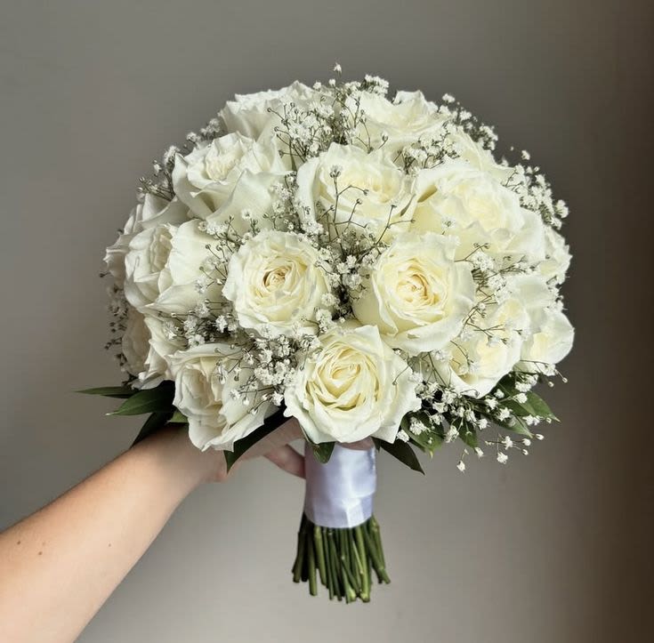 Bridal Bouquet "Angel" - A soft, romantic arrangement of ivory roses accented with delicate baby’s breath and subtle greenery. Designed with open stems and finished with an ivory satin ribbon wrap, offering a timeless, elegant look in both standard and fuller, more lush styles.