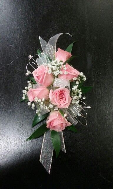 Pink rose wrist corsage with white filler flowers and sheer ribbon on a dark surface