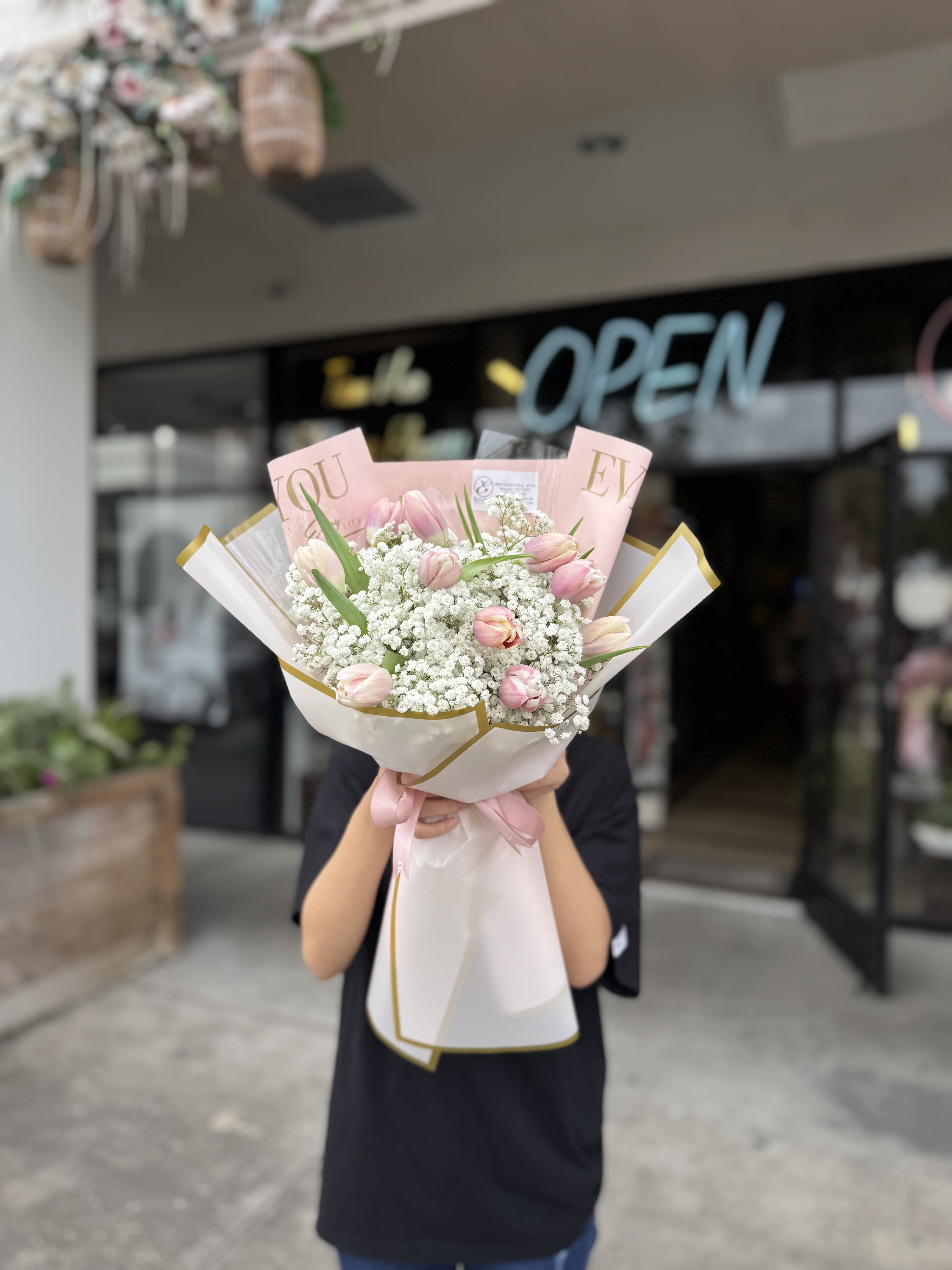 Hand-tied bouquet of light pink tulips and white filler flowers wrapped in pink and white paper with a ribbon.