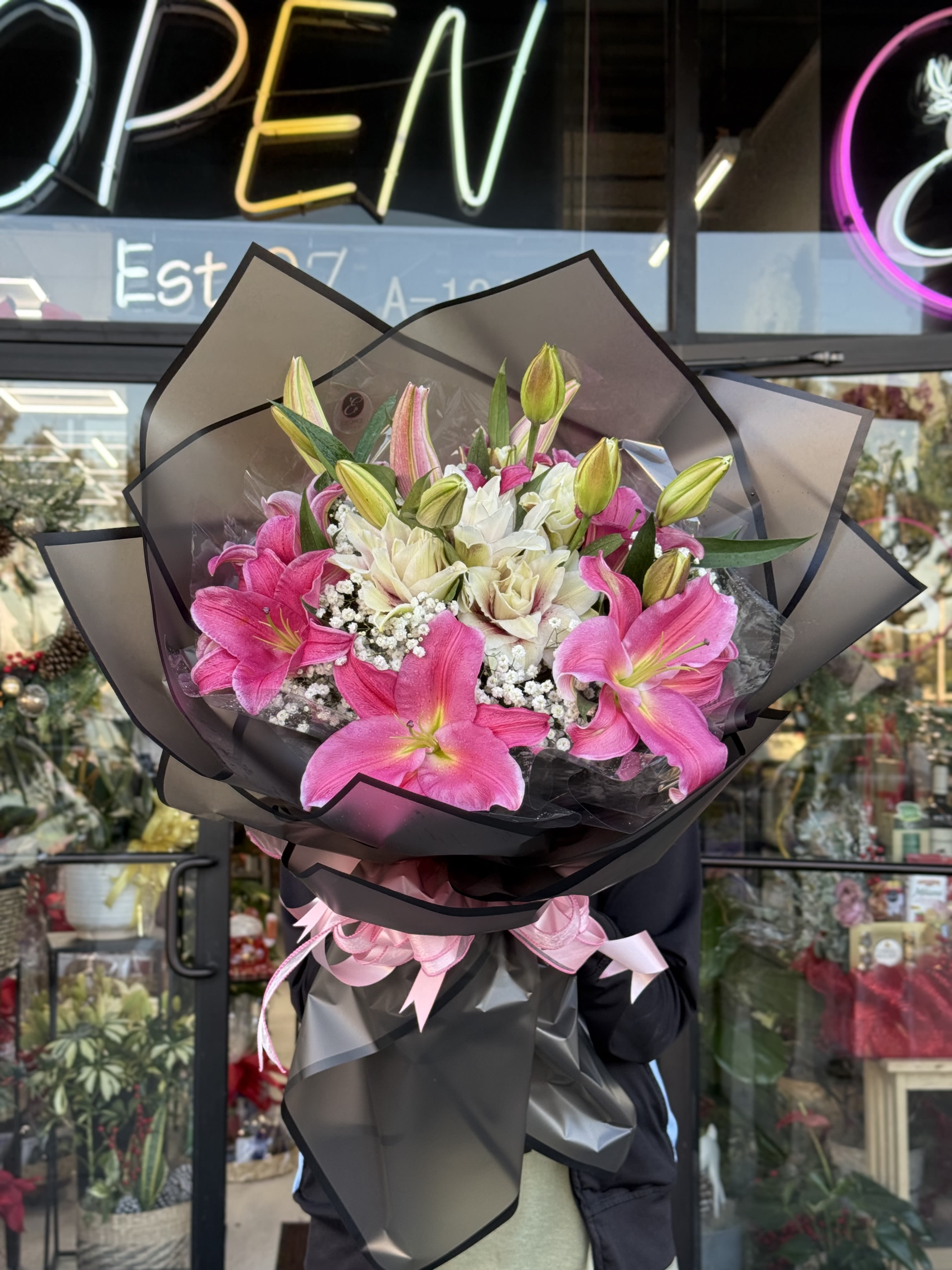 Large bouquet of pink and white lilies with baby's breath wrapped in black paper with pink ribbons