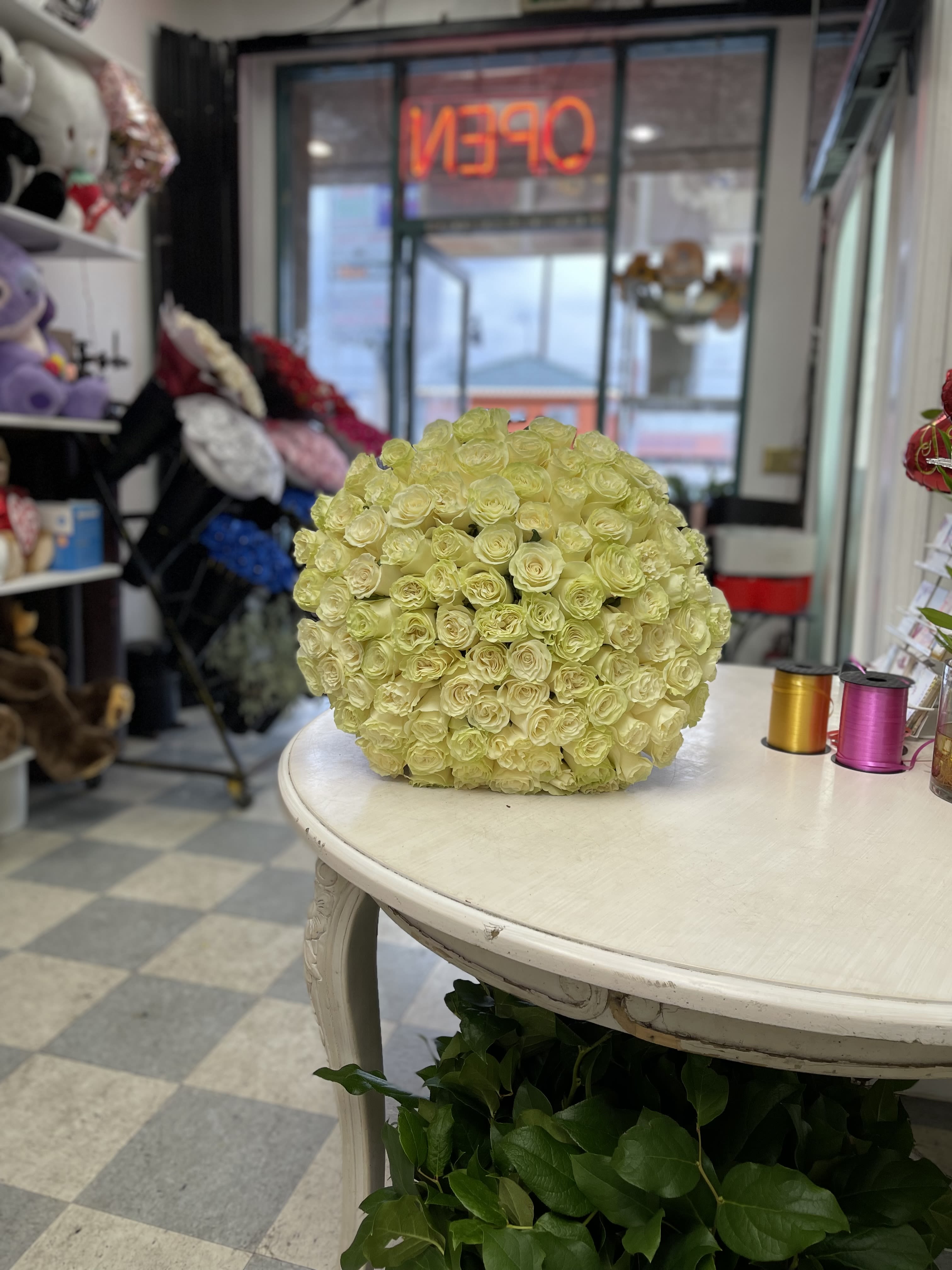 Round ball arrangement of pale yellow roses displayed on a white table in a flower shop