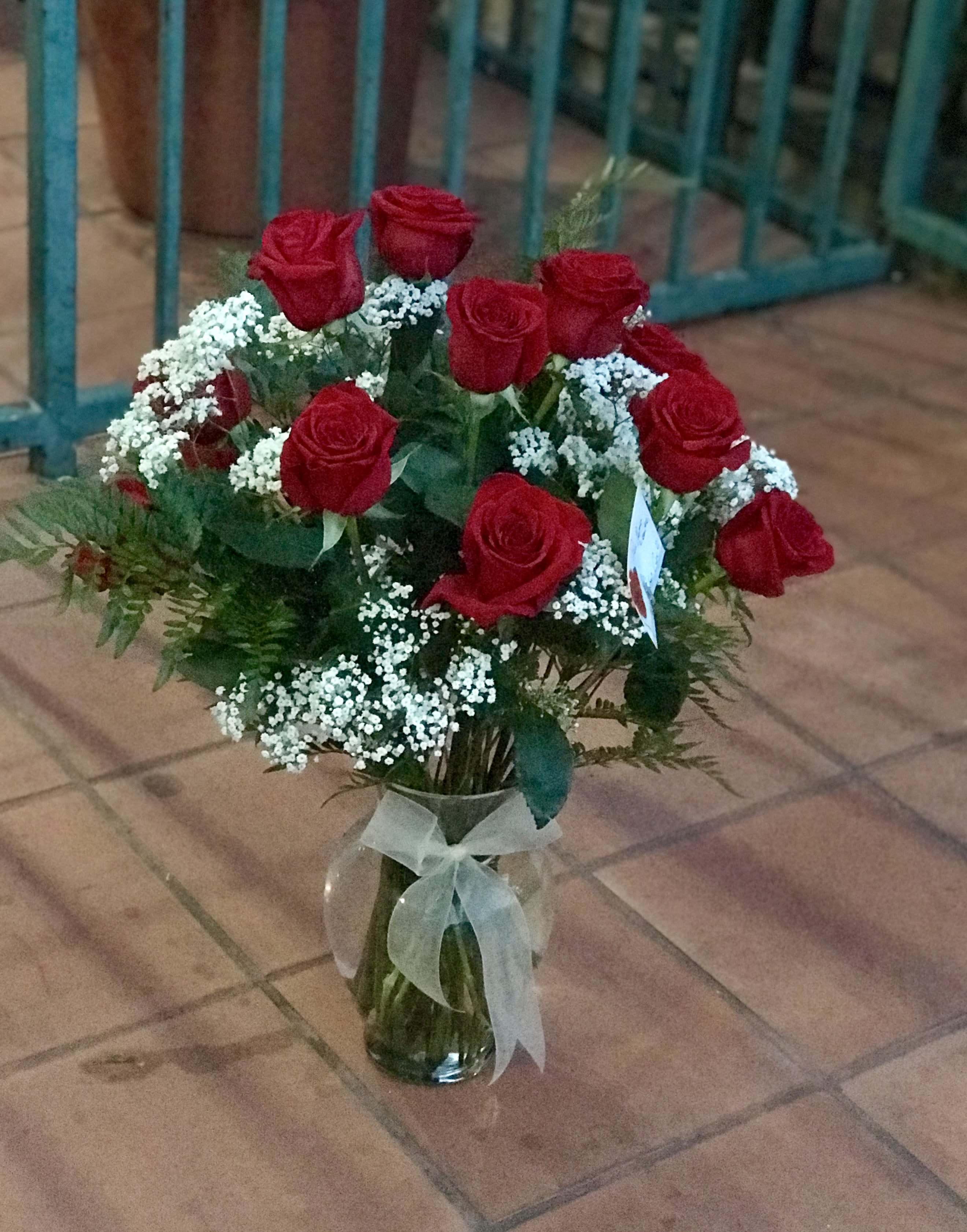 Arrangement of red roses with white filler flowers in a clear glass vase tied with a sheer bow.