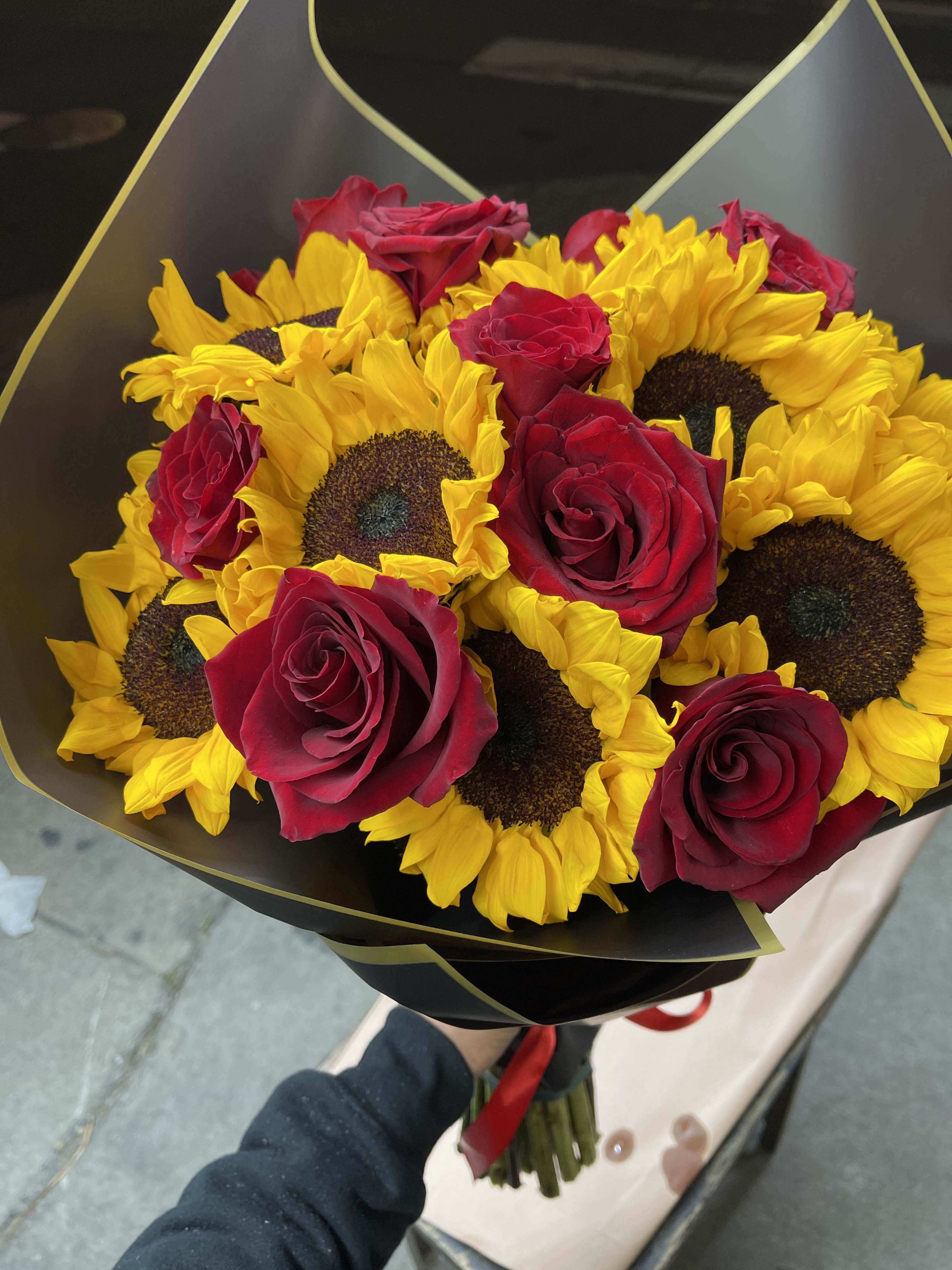 Bouquet of yellow sunflowers and red roses wrapped in black paper with gold trim.