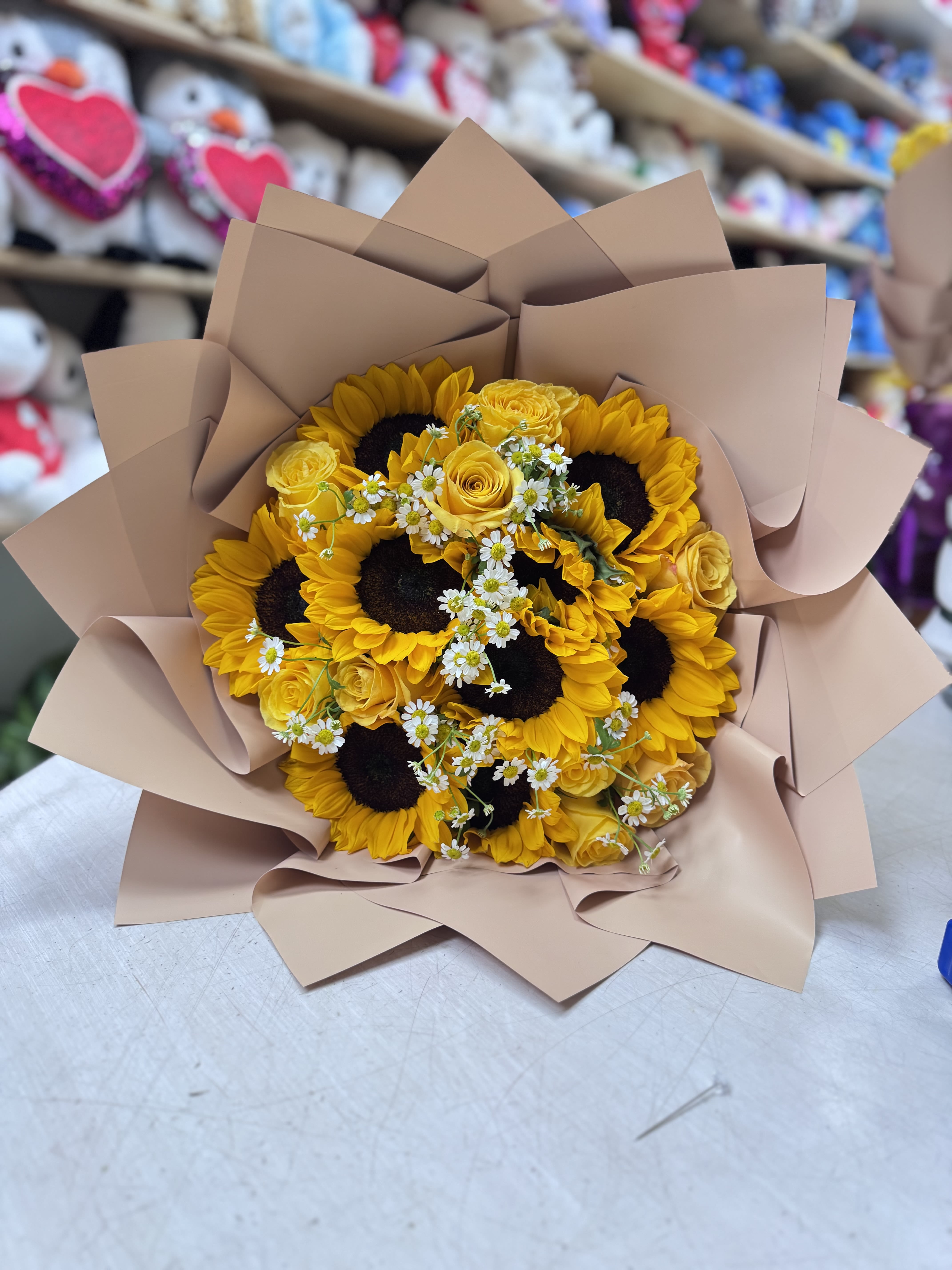 Bouquet of sunflowers, yellow roses, and small white daisies wrapped in tan paper