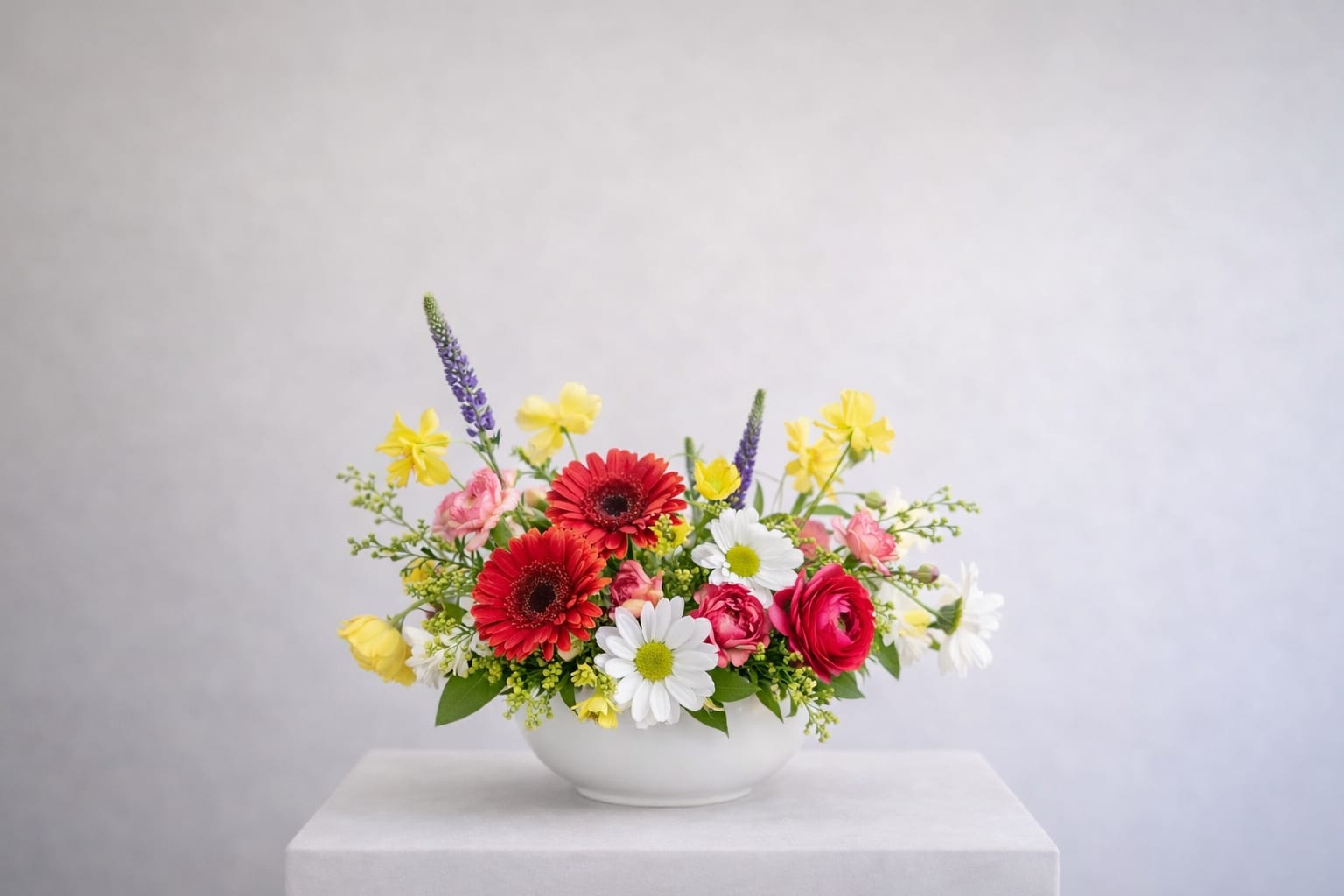 Sunlit Garden Bowl - Bright red gerbera daisies, cheerful yellow blooms, soft pink accents, and crisp white florals come together in a lively, garden-inspired arrangement.  Designed with an airy, organic feel, this smaller piece still offers beautiful movement and texture while fitting perfectly on side tables, desks, or intimate dining settings. It’s a fresh burst of color that brings warmth and happiness to any space—effortlessly.  Perfect for everyday gifting, thank-yous, or a simple moment of beauty. 