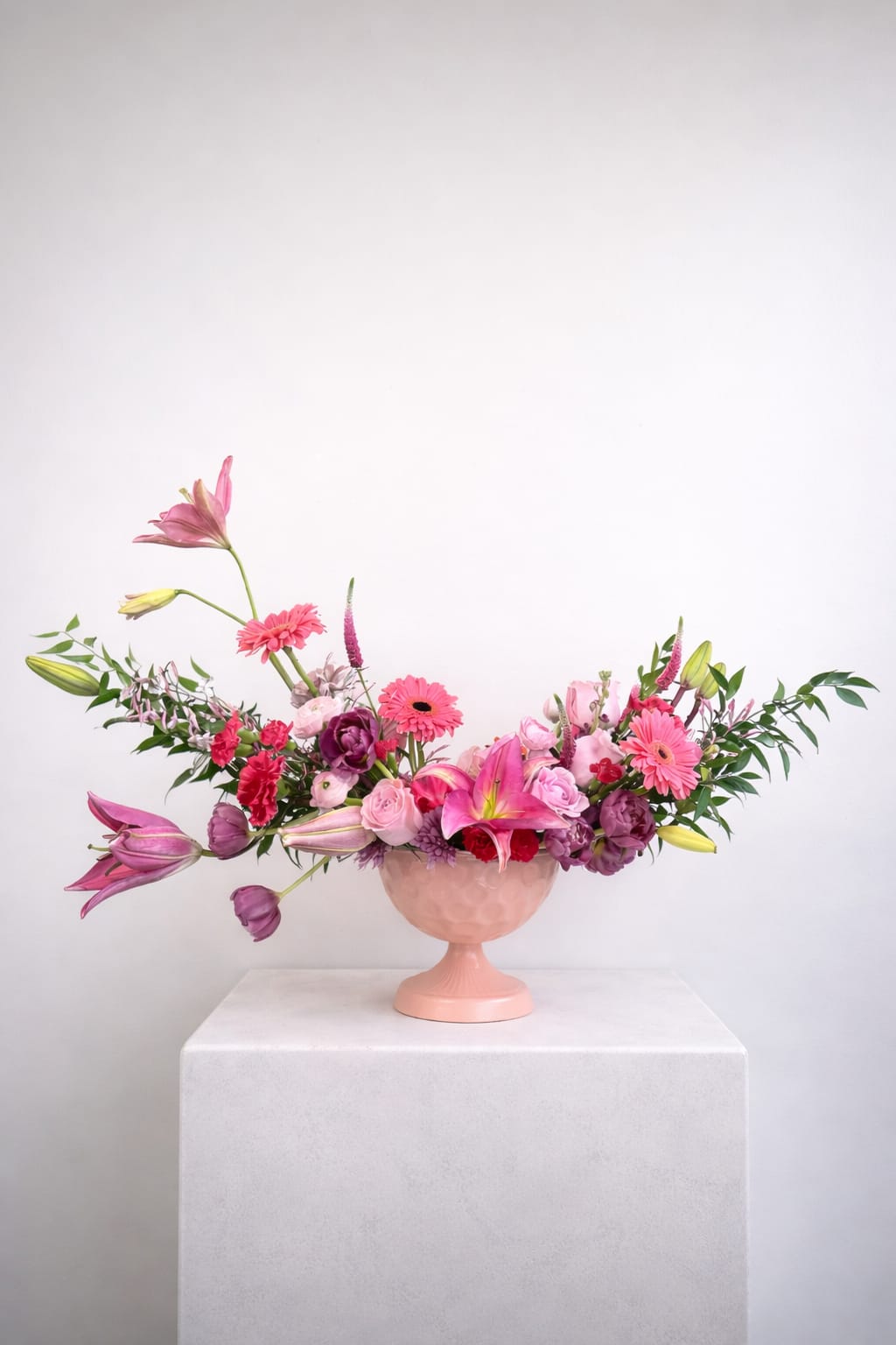 Pretty In Pink - Designed with an airy, garden-inspired silhouette, this arrangement features layers of soft blush and vibrant pink blooms—from striking lilies and playful gerbera daisies to delicate roses and textural accents.  Gracefully extending outward with natural movement, each stem feels intentionally placed yet effortlessly organic. The soft pink vessel complements the palette, enhancing the overall sense of cohesion and charm.  Perfect for celebrations, thoughtful gifting, or adding a touch of elegance to any space, this piece is both whimsical and refined—an ode to all things pink.