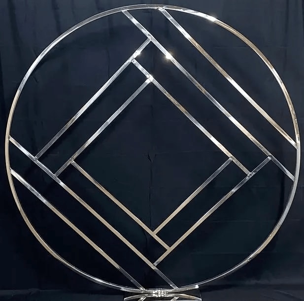 Aztec Round Backdrop - Silver - Create your own backdrop or focal point at your event. This metal circle arch is a beautiful addition to your event covered in florals, greenery or balloons. Lightweight metal is easily weighted with sand bags (not included). 6ft Tall 6ft Wide Ordering online is not available. Call or email to inquire availability and additional fees.