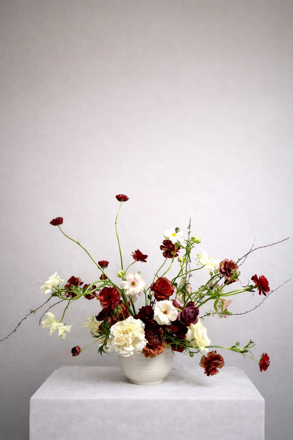Scarlet Reverie - Deep crimson and burgundy blooms weave through soft ivory florals, creating a rich, layered composition that feels both untamed and refined.  Delicate, airy stems extend outward with an organic rhythm, giving the arrangement a sculptural silhouette that feels almost like it’s unfolding in real time. The interplay of light and dark tones adds depth and intrigue, while the minimal vessel keeps the focus entirely on the florals.  Perfect for those drawn to a more artistic, editorial style, this piece brings a sense of romance and modern edge to any space.