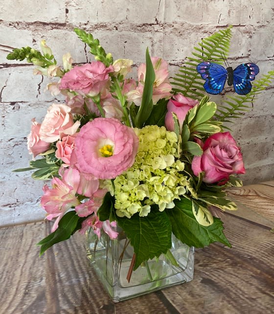 “KERRI” - A sweet cube vase arrangement filled with roses, lisianthus, hydrangea, snapdragons and premium accent flowers and foliage. A “flutterby” adds a bit of whimsy to the design.