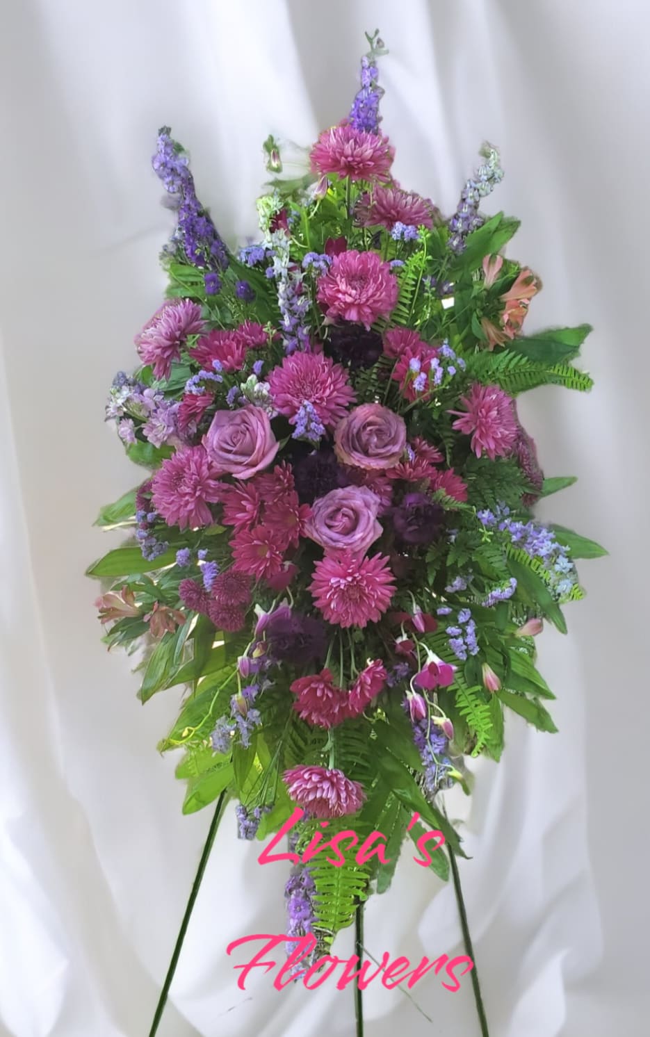 Tall standing spray of purple roses and pink mums arranged in a cascading shape on an easel.