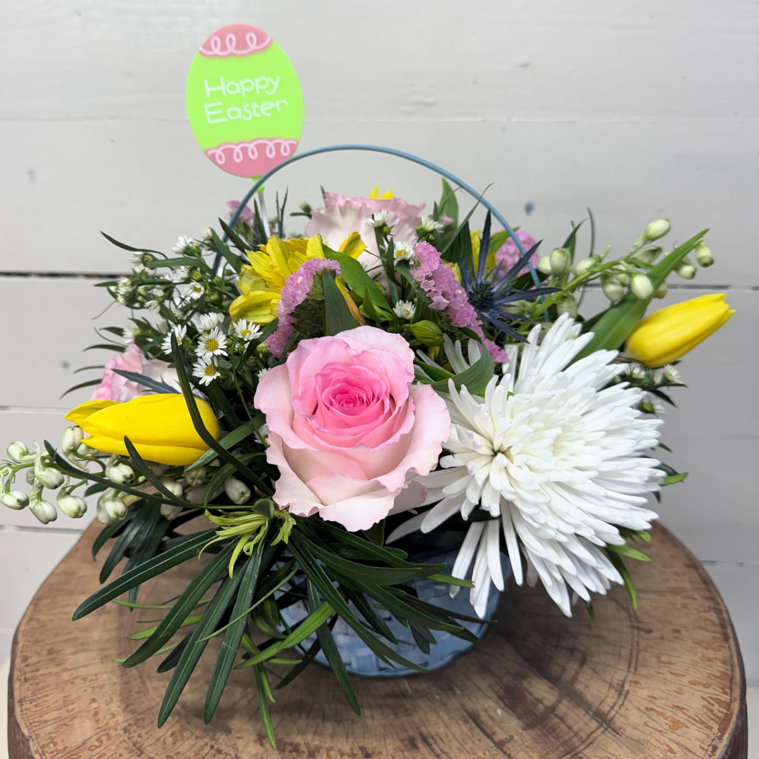Low Easter flower arrangement with pink rose, yellow tulips, and white mum in a blue bucket