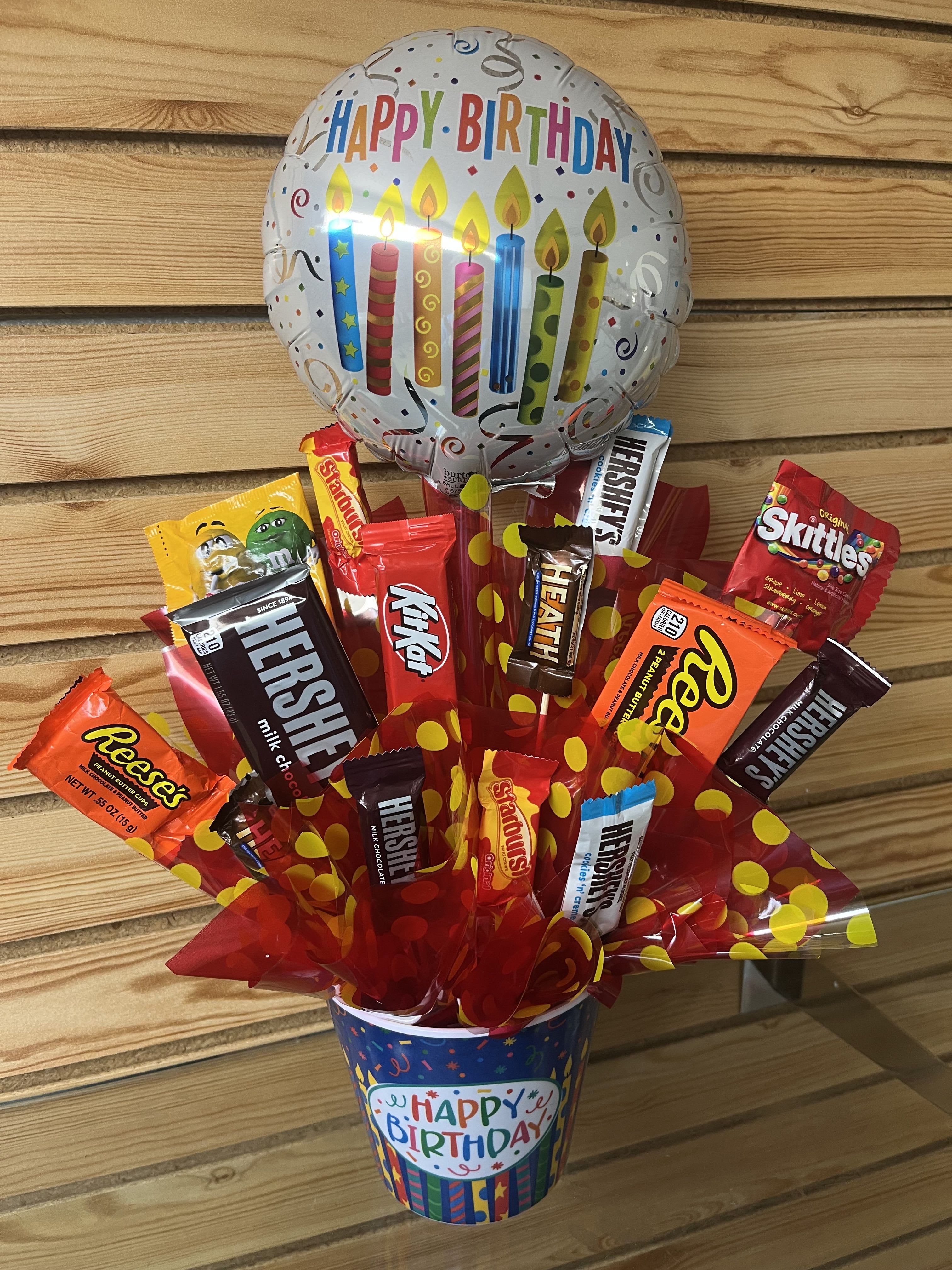Birthday candy bouquet in a festive cup with assorted chocolate bars and a Happy Birthday balloon.