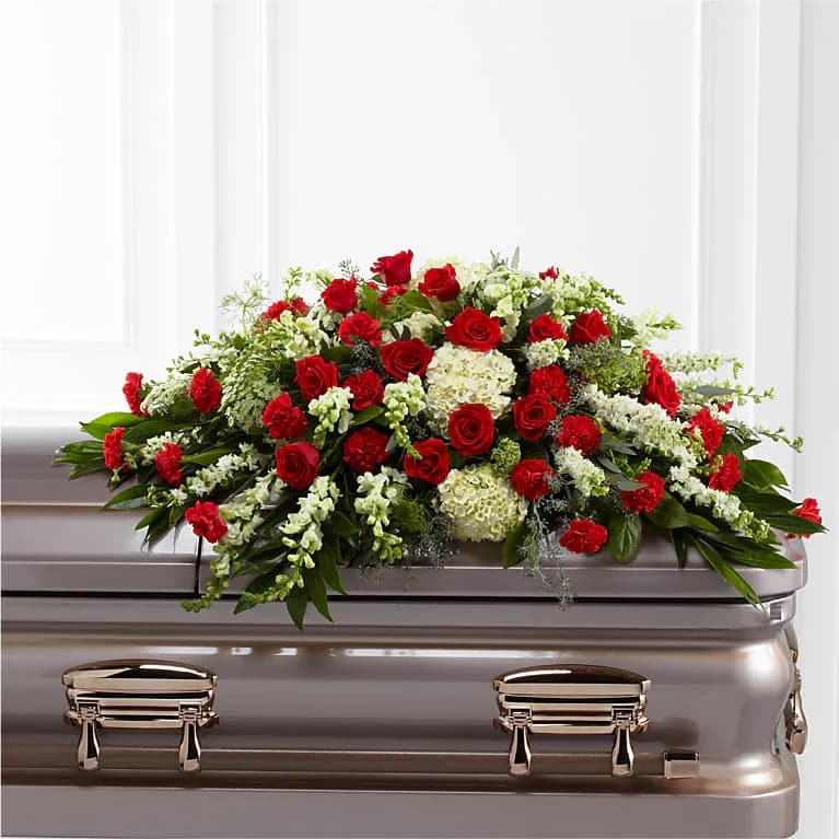 Red and white casket spray with roses, carnations, hydrangeas, and snapdragons atop a metallic casket