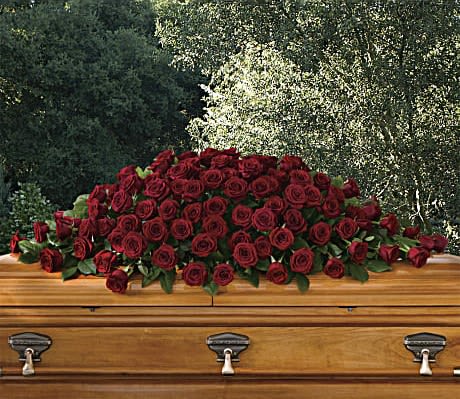 Large spray of dark red roses arranged on top of a wooden casket outdoors