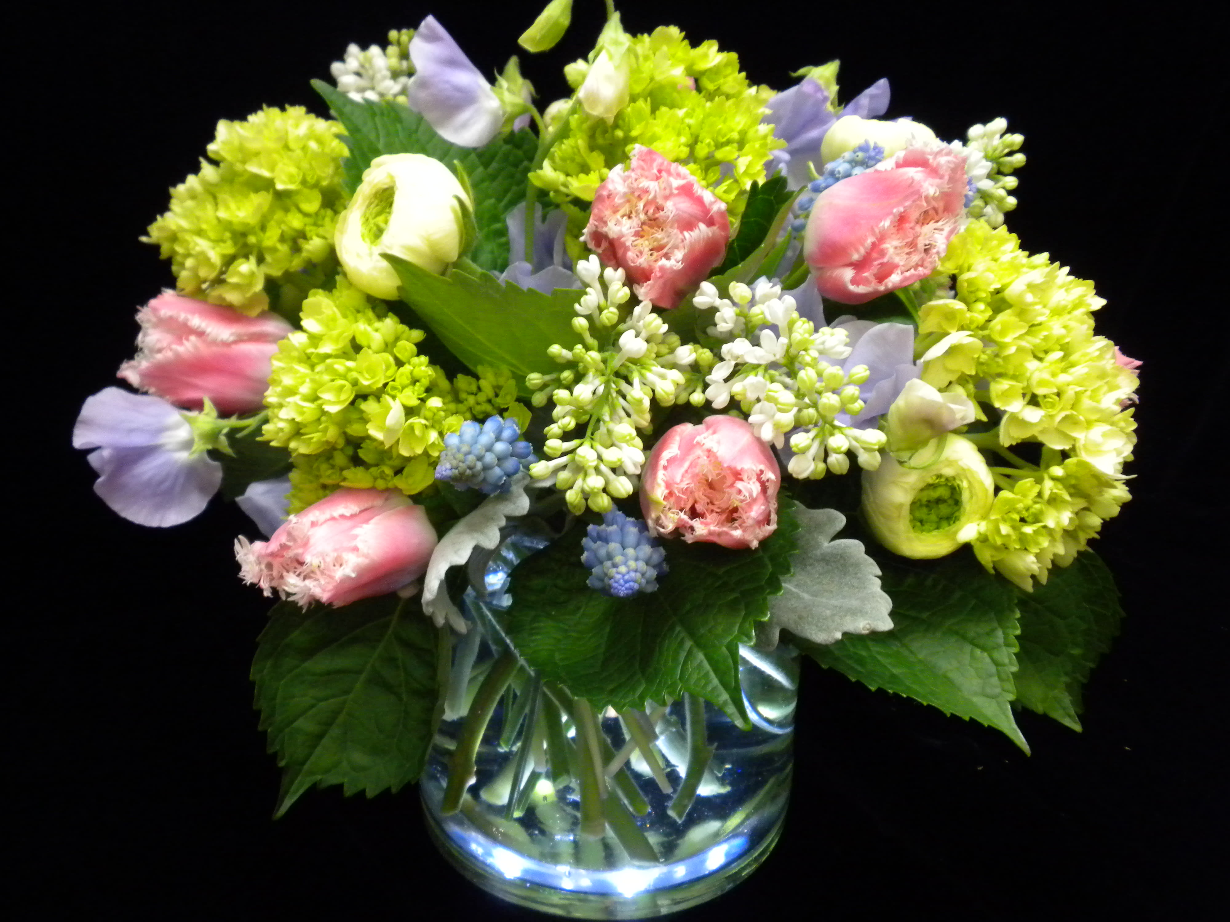 Low glass vase of pink fringe tulips, green hydrangeas, lilac, and pastel blooms in a rounded arrangement