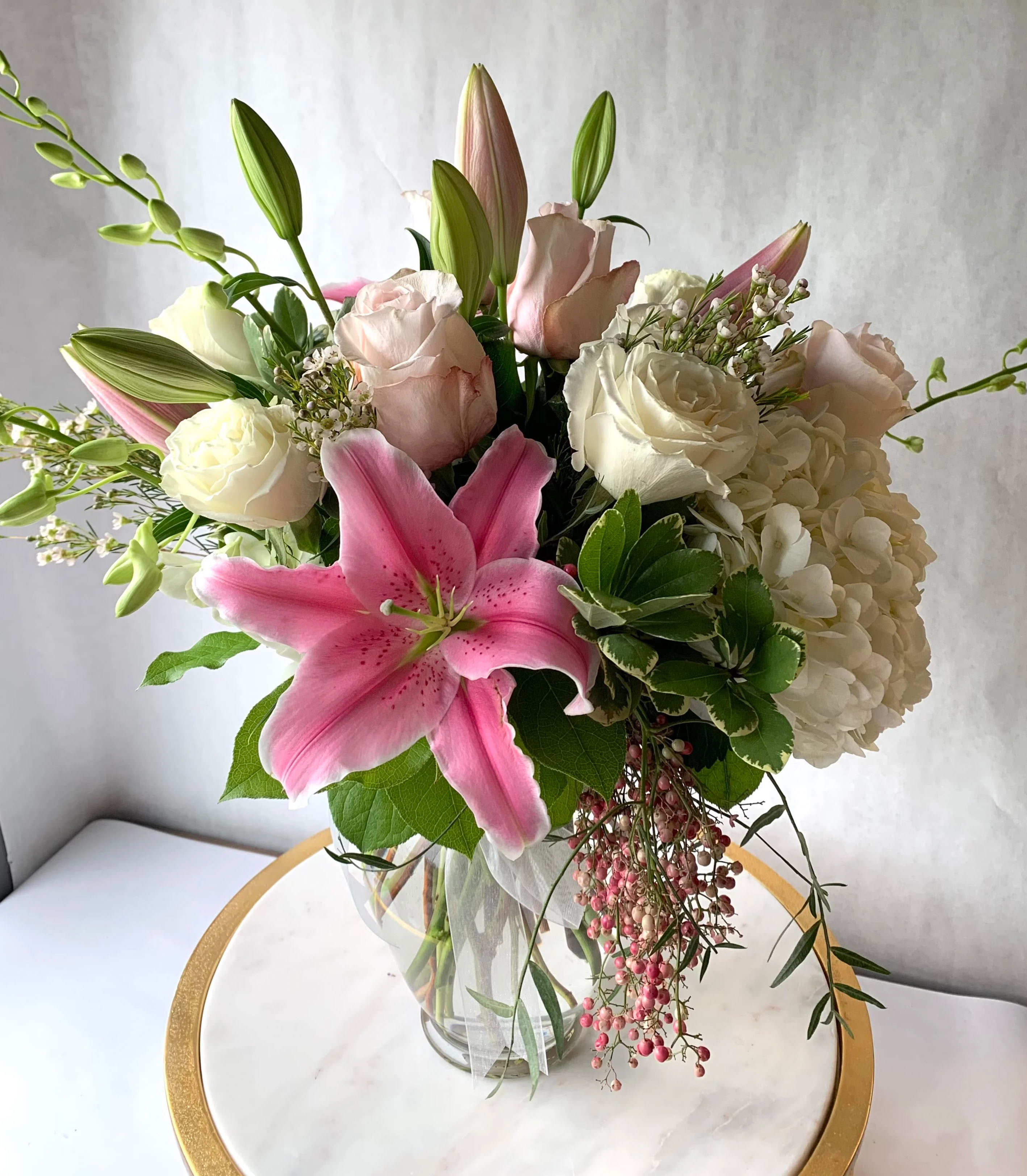 Pink lily, white hydrangea, and pale roses arranged in a clear glass vase