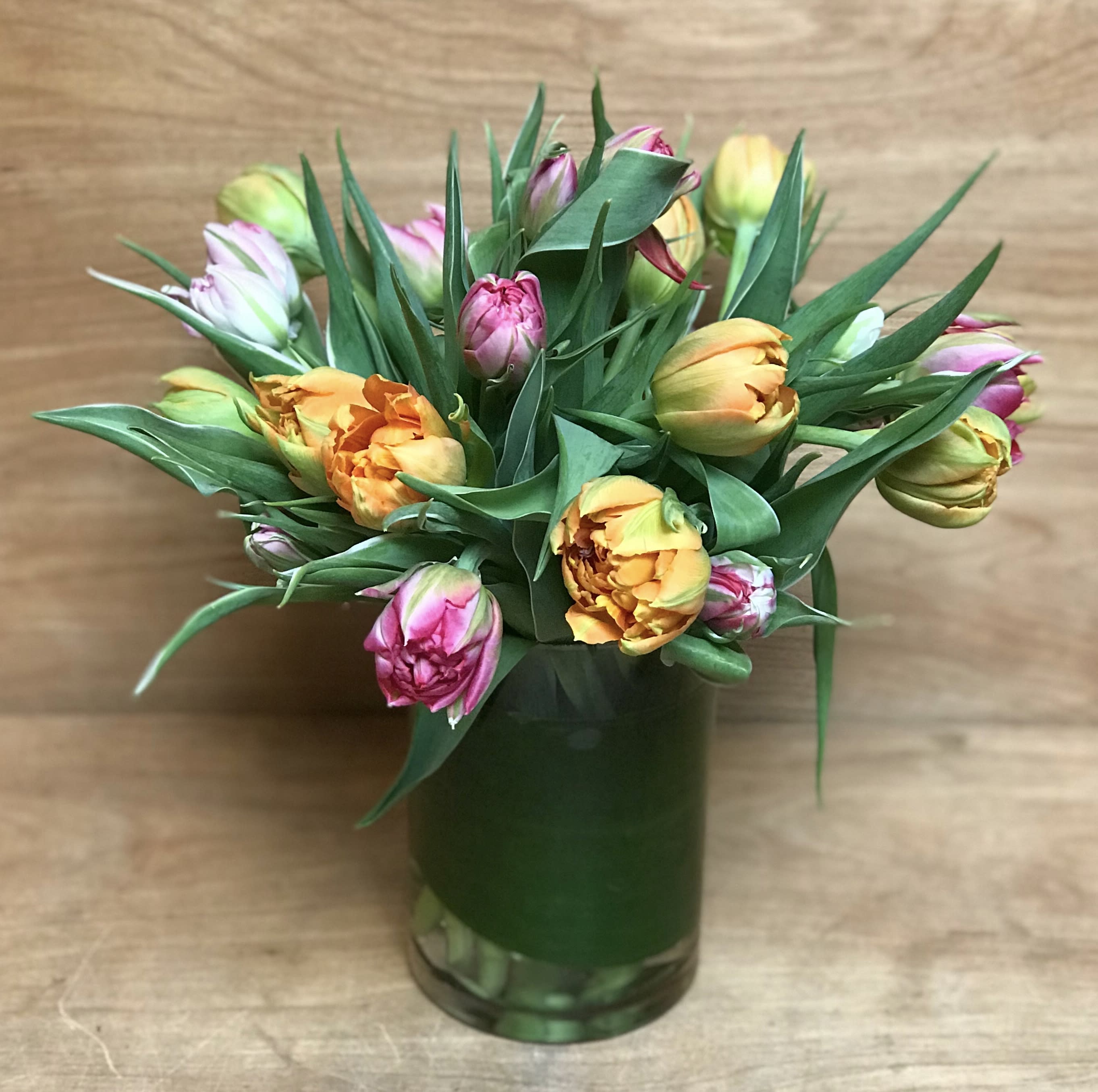 Arrangement of yellow and pink tulips in a leaf-wrapped clear glass vase